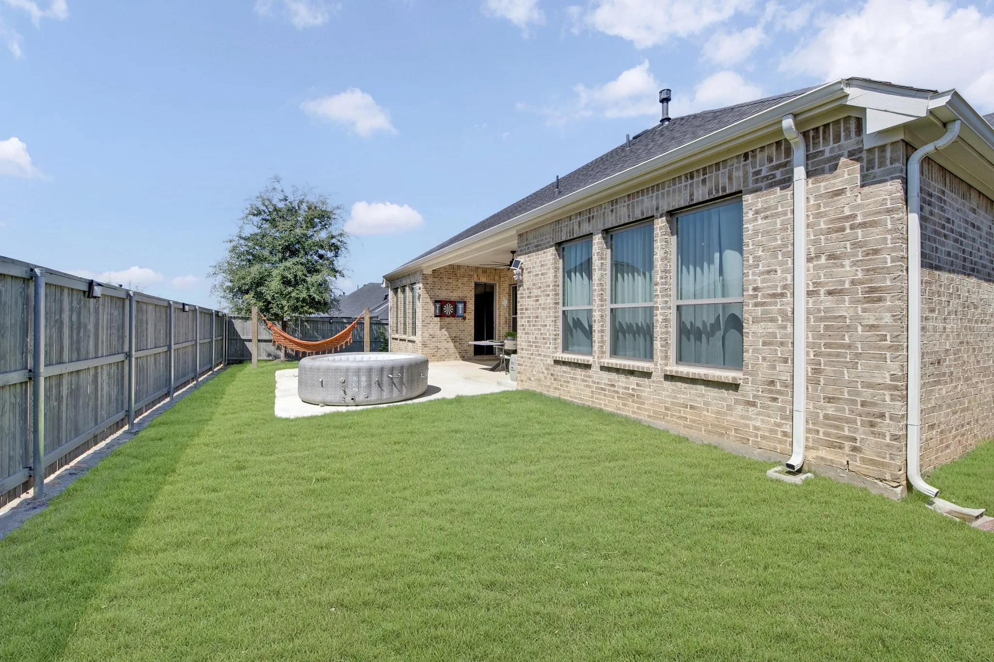 Expansive lawn area with a wood privacy fence, concrete patio, and brick exterior