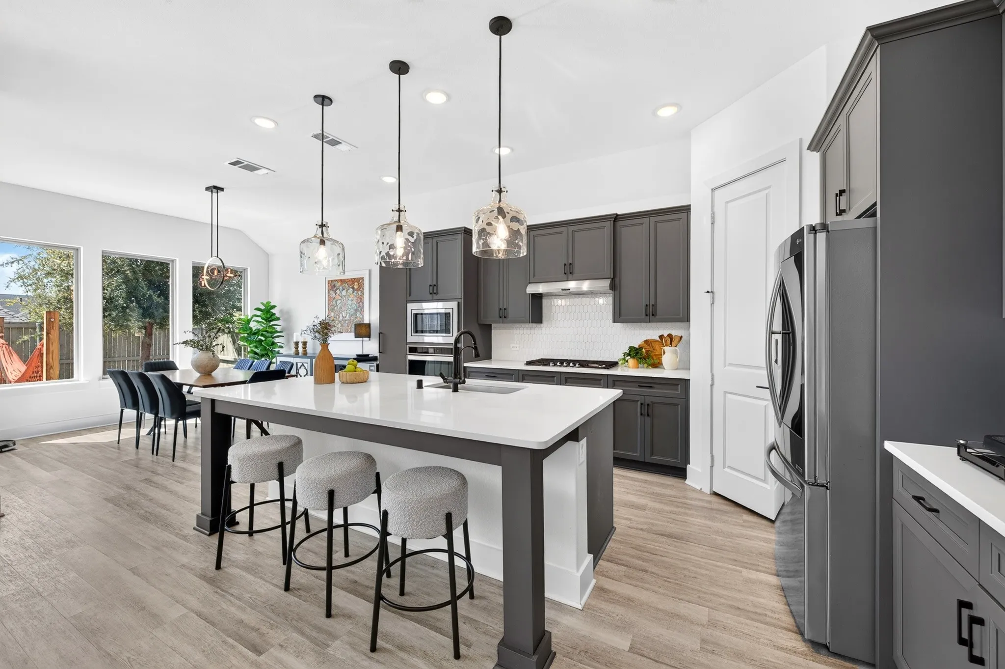 Open-concept kitchen with a large central island, dark gray cabinetry, stainless steel appliances, and wood-finish flooring