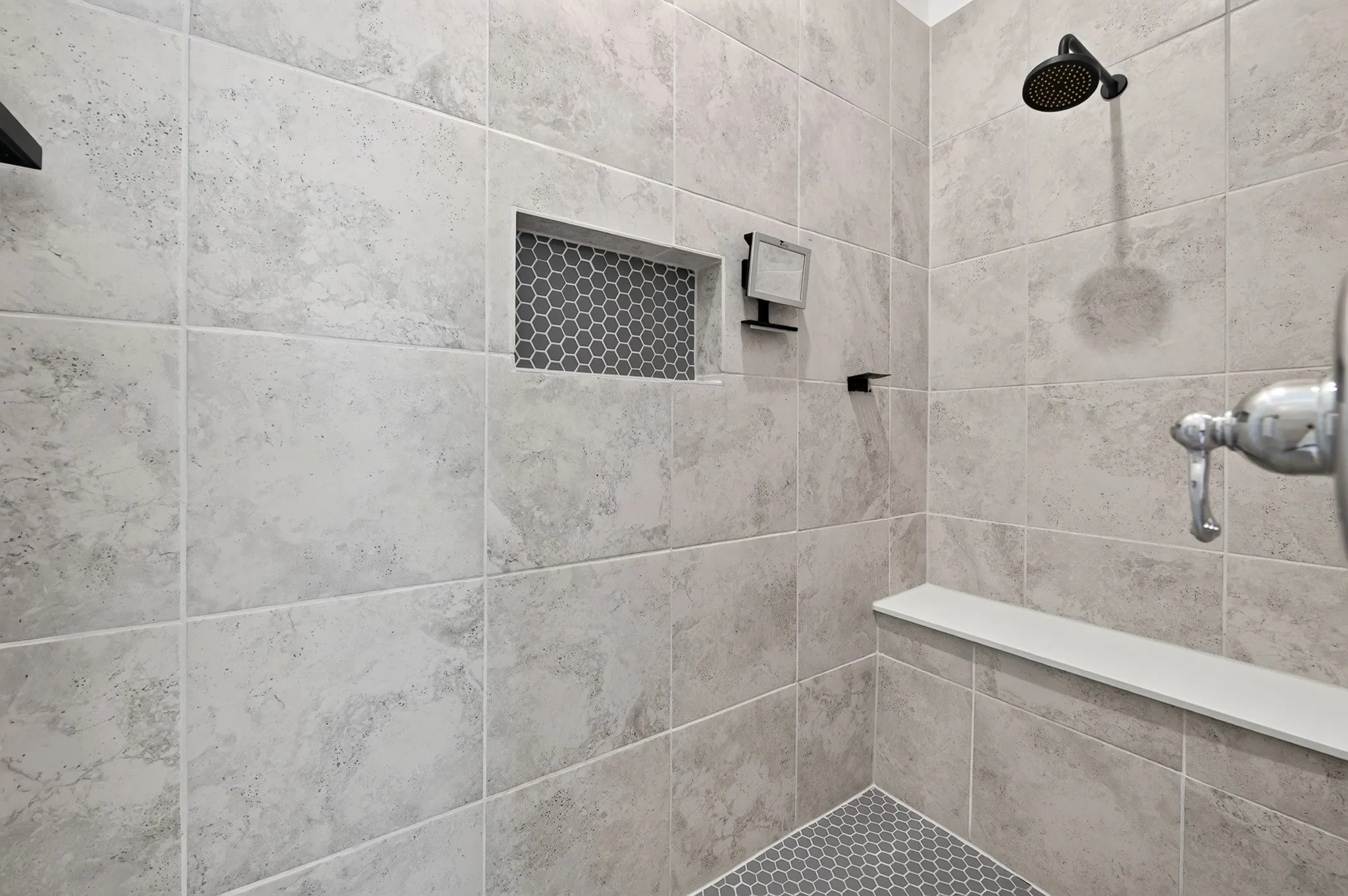 Tiled shower with a built-in niche featuring hexagonal mosaic tile, a white shower bench, and a matte black rain shower head
