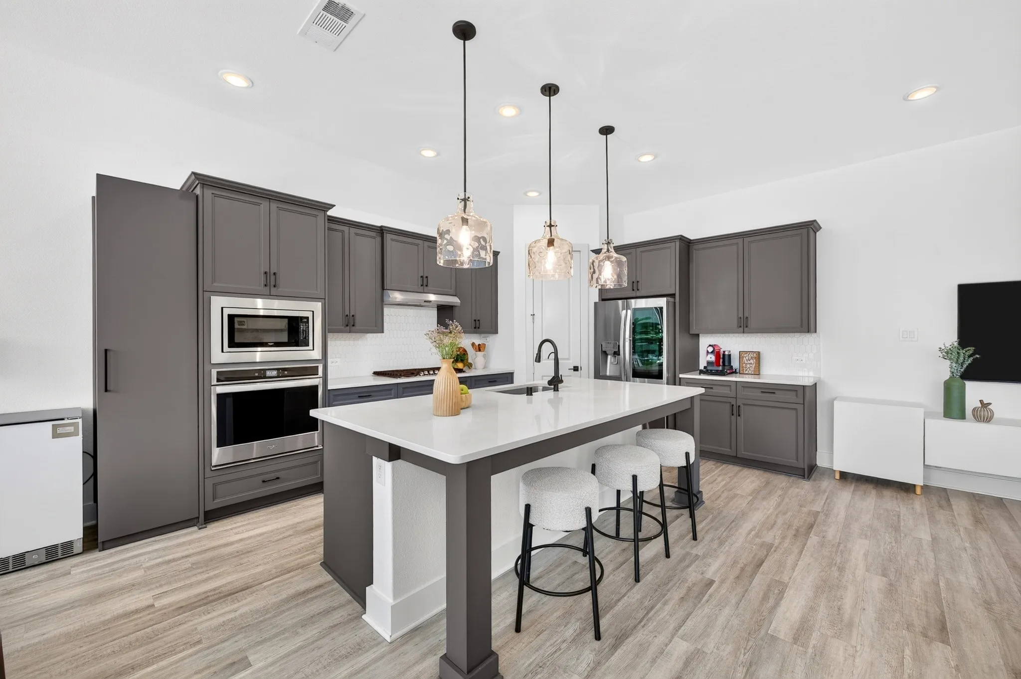 Kitchen featuring wood-finish flooring, recessed lighting, a central island with a white countertop, dark gray cabinetry, and stainless steel built-in appliances
