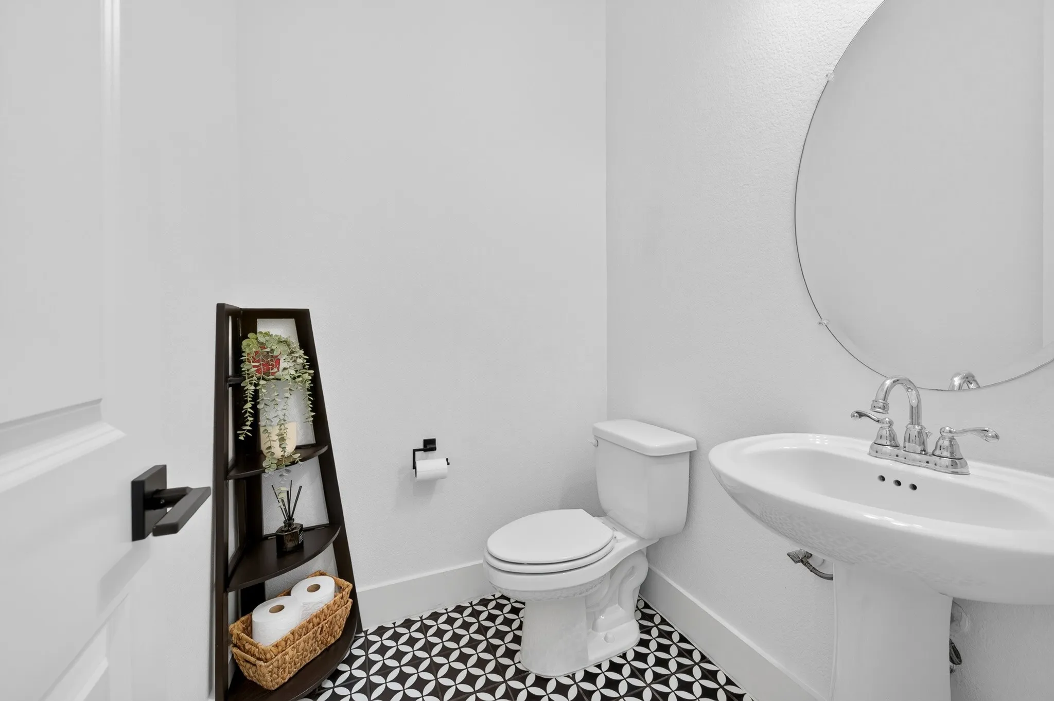 Pedestal sink with chrome fixtures, round wall-mounted mirror, and patterned floor tile
