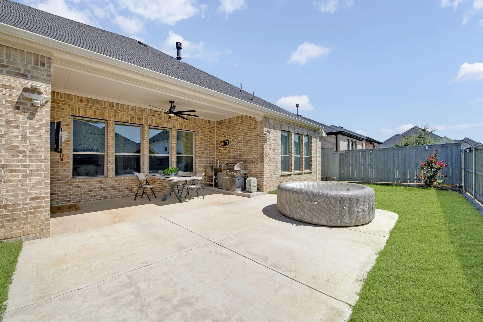 Covered patio with a ceiling fan, brick exterior, multiple windows, concrete patio, and a grassy yard