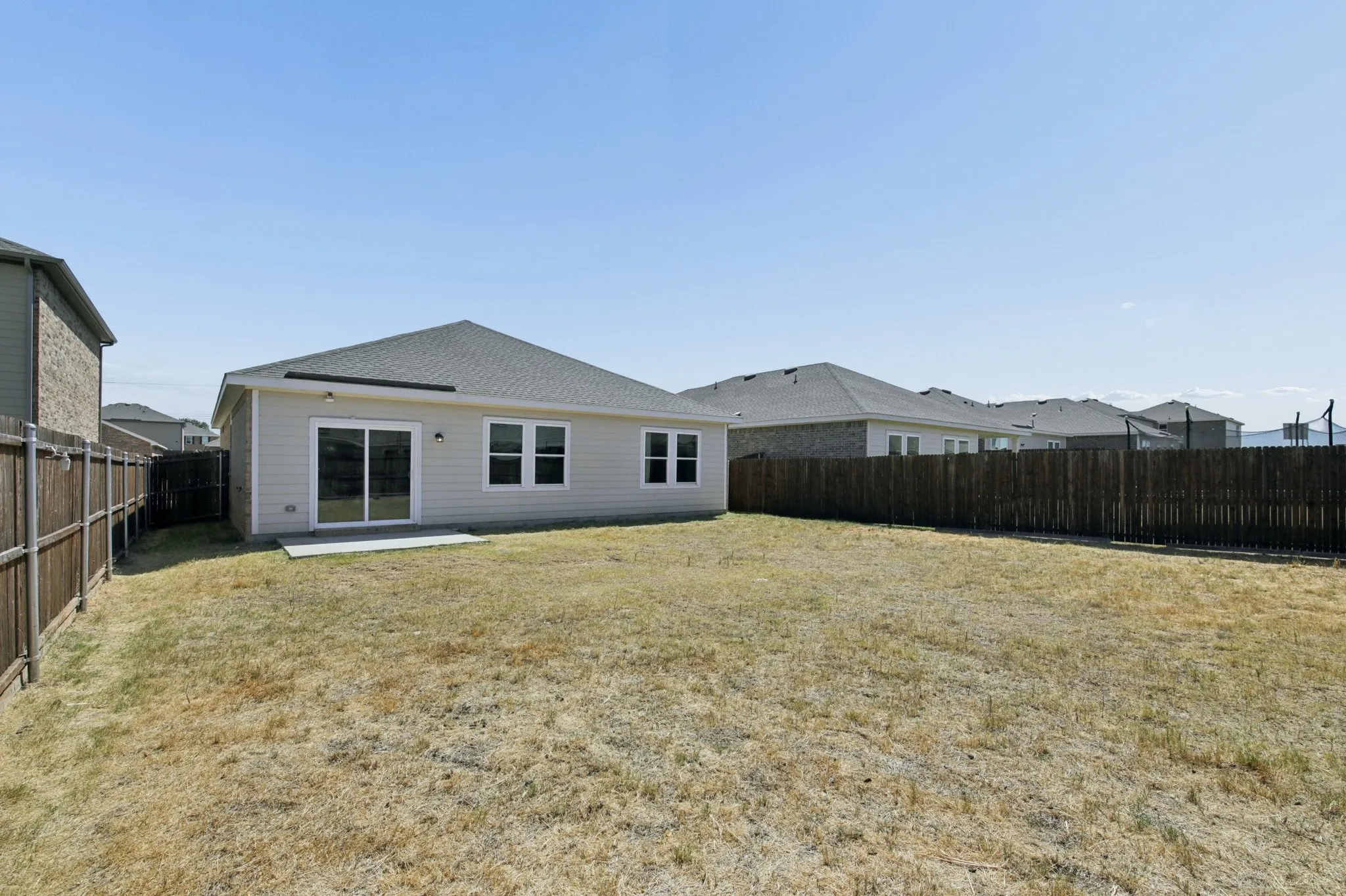 Large backyard has grass and wood fencing.