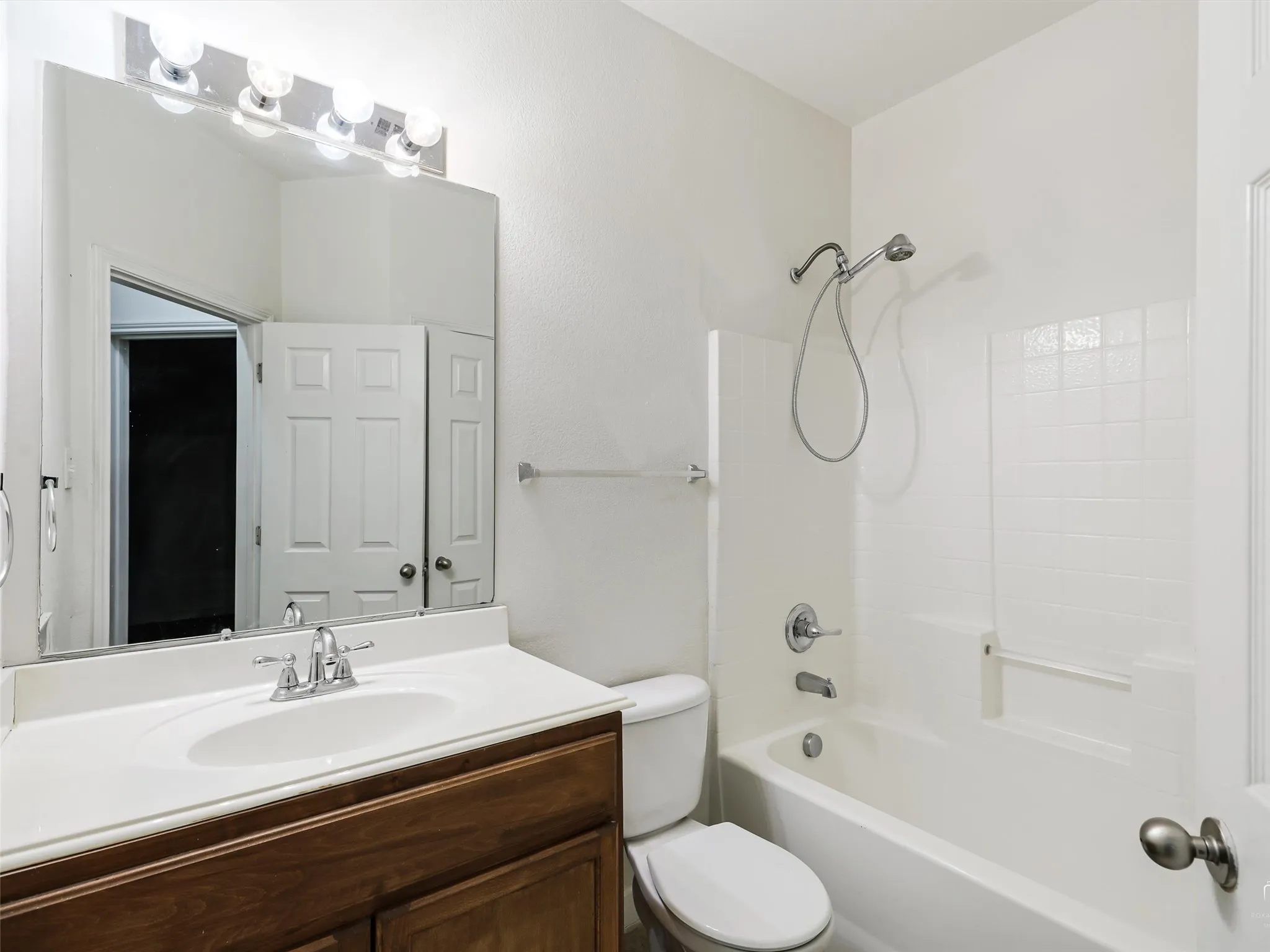 Bathroom featuring a wood-finish vanity with an integrated sink, polished chrome faucet, and a large mirror with overhead vanity lighting
