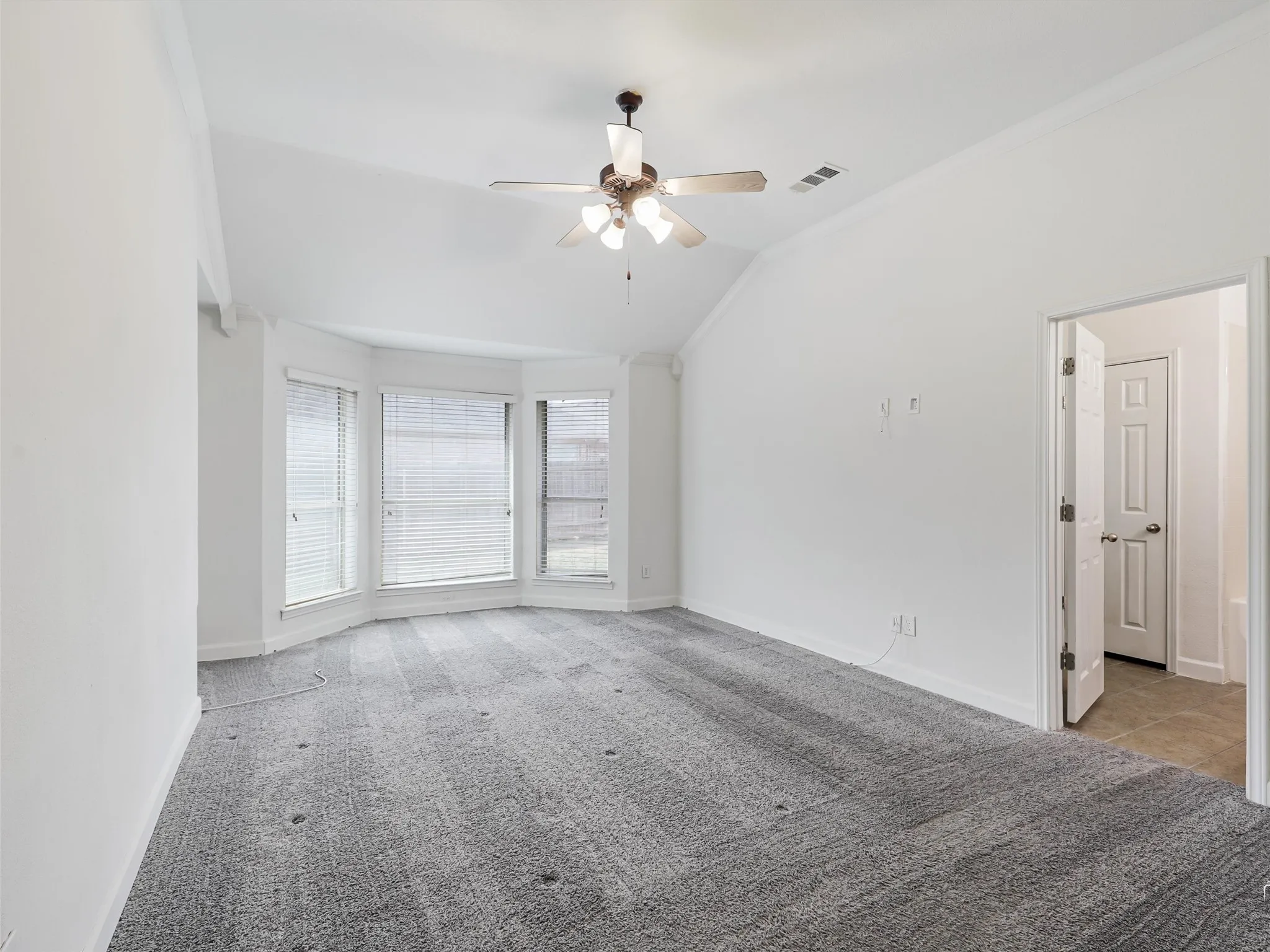 Vaulted ceiling with a ceiling fan, bay window with blinds, and light gray patterned carpet