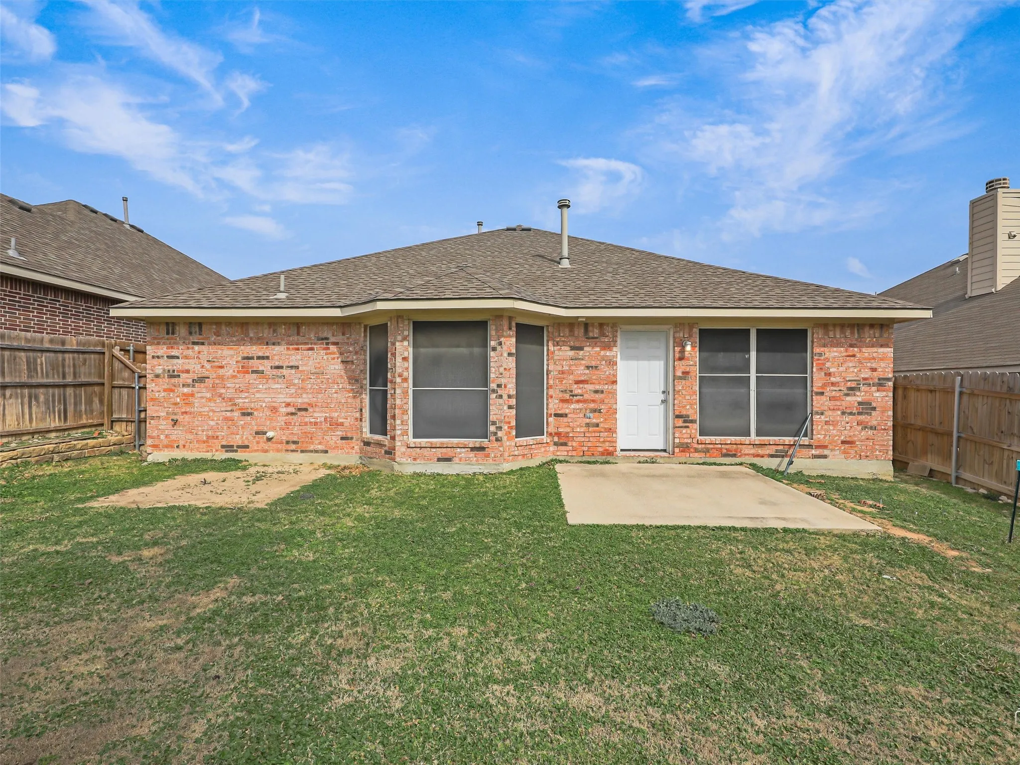 Rear exterior featuring a brick facade, multiple windows, a white door, and a concrete patio