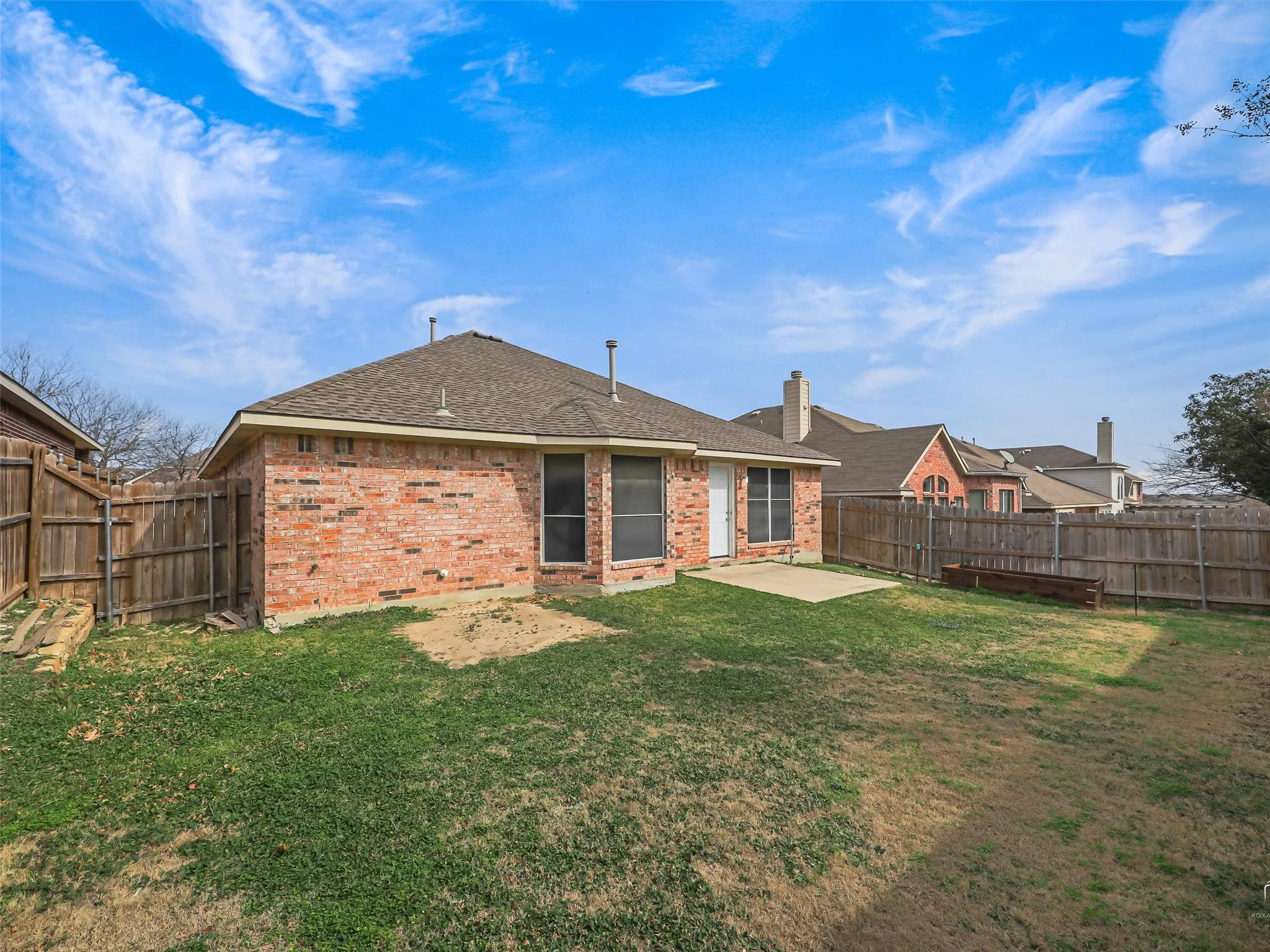 Expansive backyard featuring a brick exterior, privacy fencing, and a concrete patio