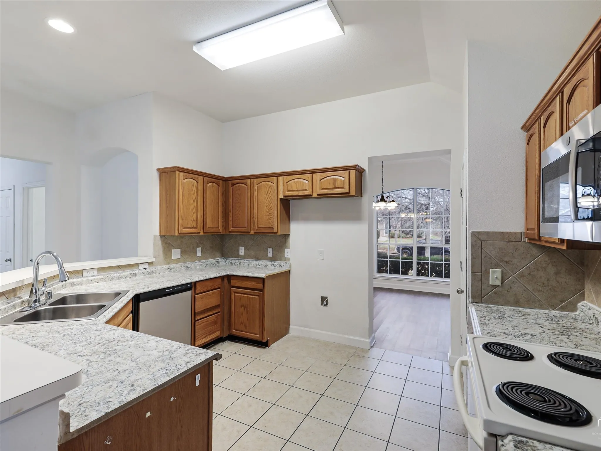Kitchen featuring wood cabinetry, stone-look countertops, a stainless steel double basin sink, and tile flooring