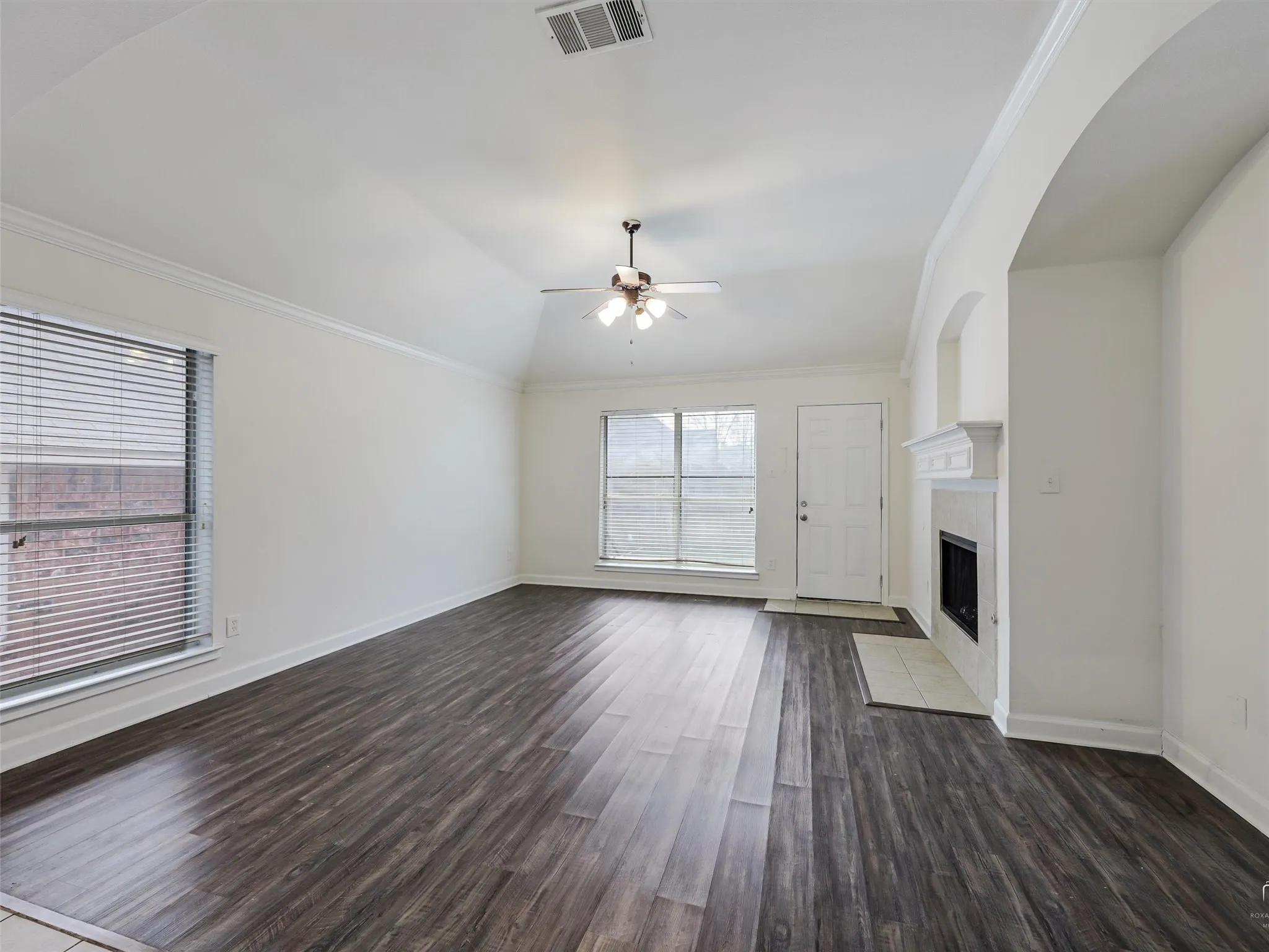 Vaulted ceiling, wood-finish flooring, two windows, fireplace with tile hearth, and an arched entryway