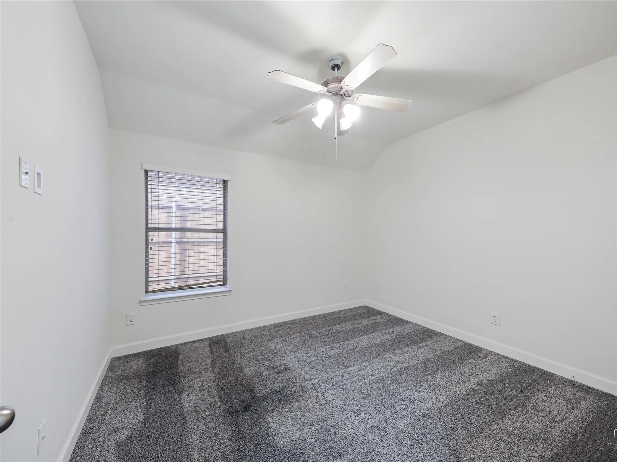 Vaulted ceiling with a ceiling fan, neutral wall paint, window with blinds, and textured gray carpeting