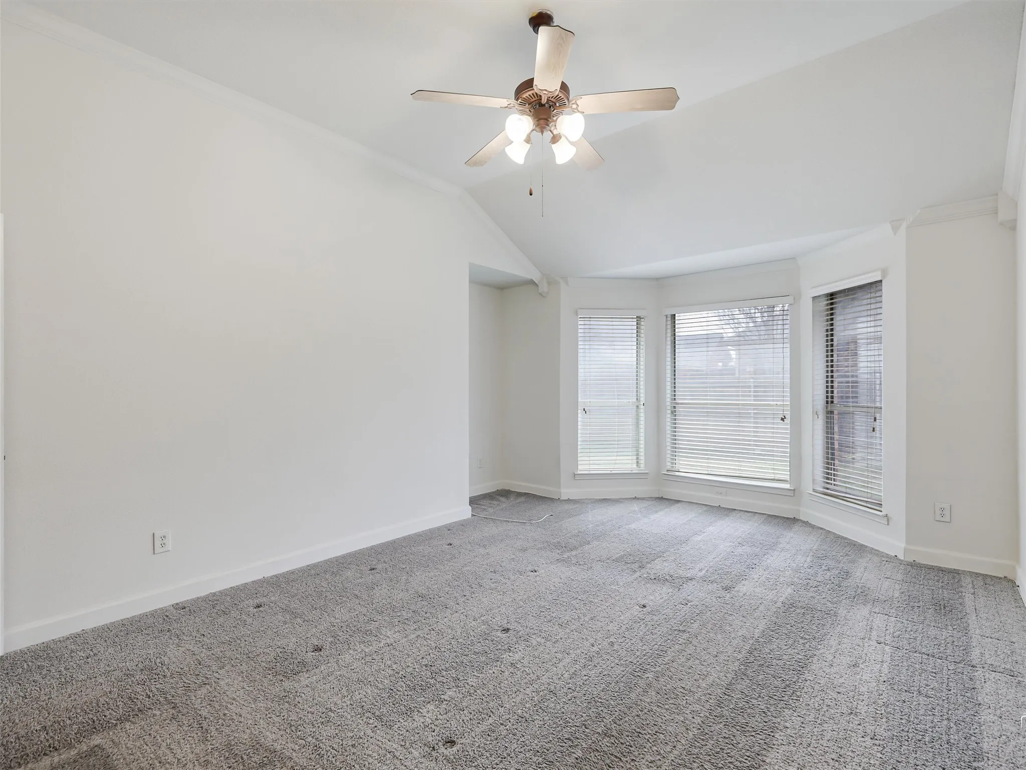 Vaulted ceiling with crown molding, ceiling fan with integrated lighting, bay window with blinds, and carpet flooring