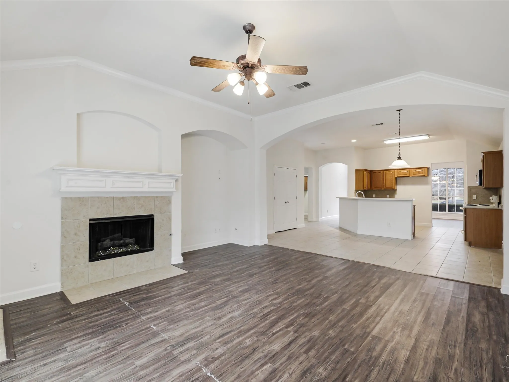 Spacious room featuring wood-finish flooring, a ceiling fan, a fireplace with a decorative mantel and tile surround, and arched openings