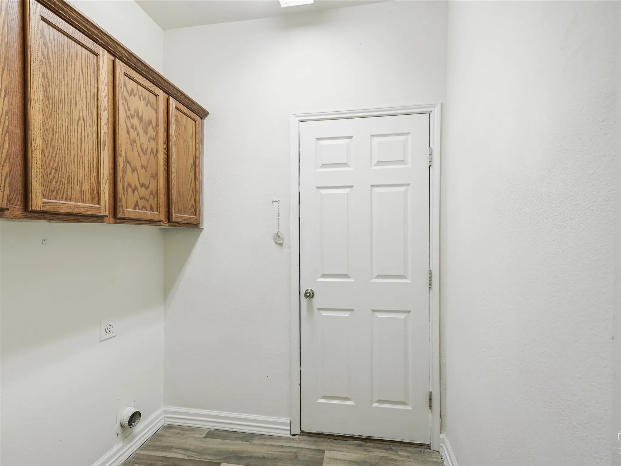 Utility room featuring oak wood-finish cabinetry with ample storage, wood-finish flooring, recessed ceiling lighting, and a six-panel white entry door with brushed nickel hardware