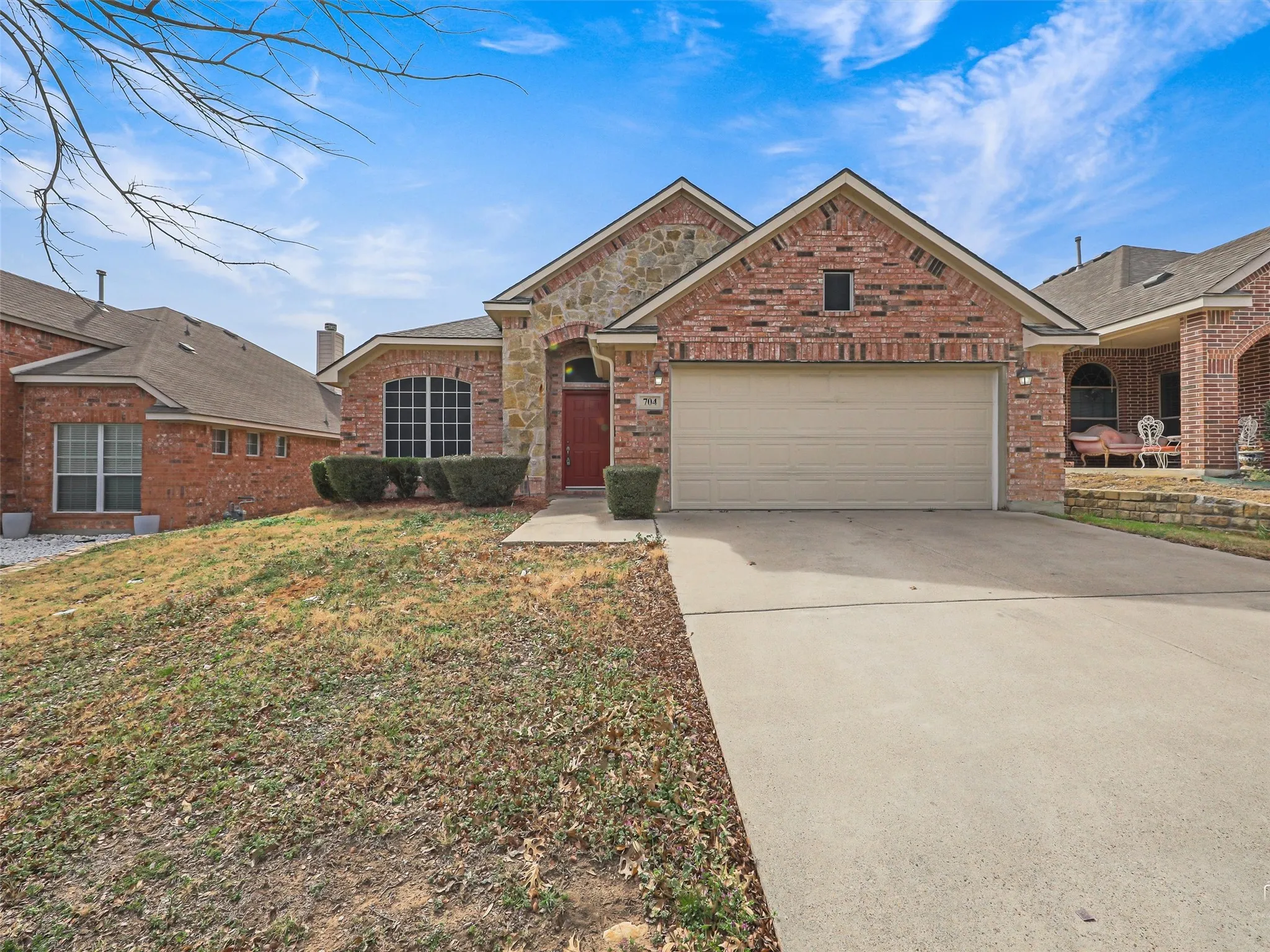 Brick and stone exterior with an arched entry, two-car garage, and established front landscaping