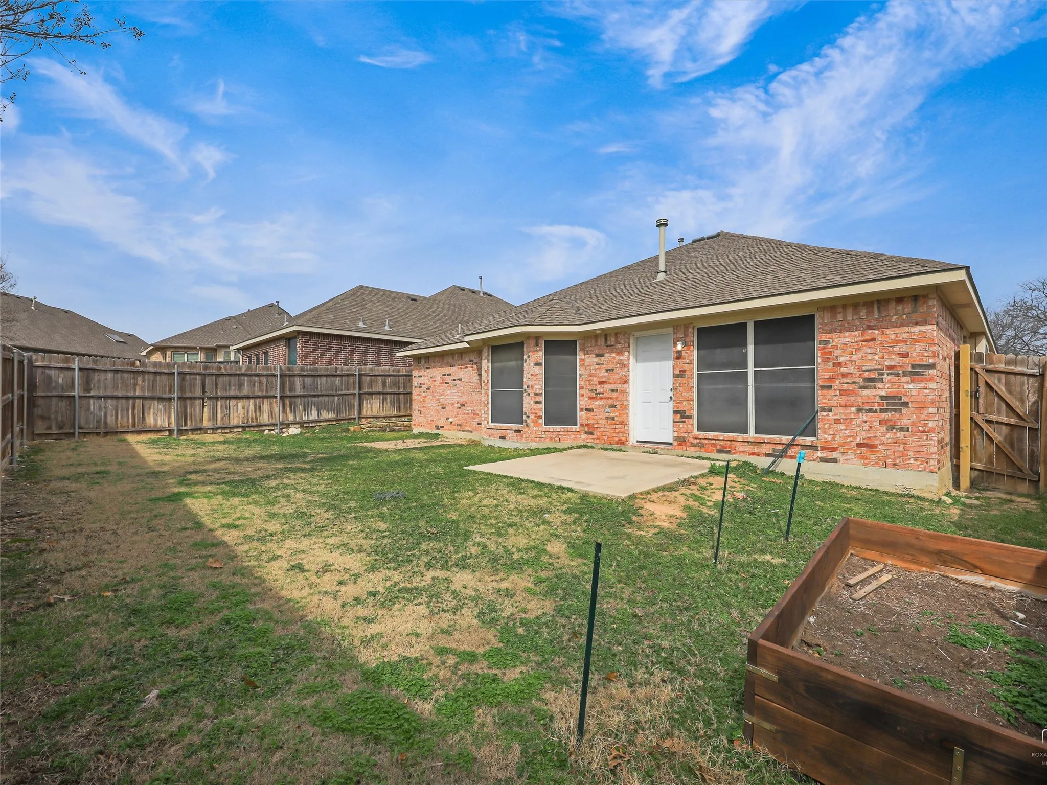 Expansive backyard featuring a privacy fence, concrete patio, brick exterior, and a built-in planter box