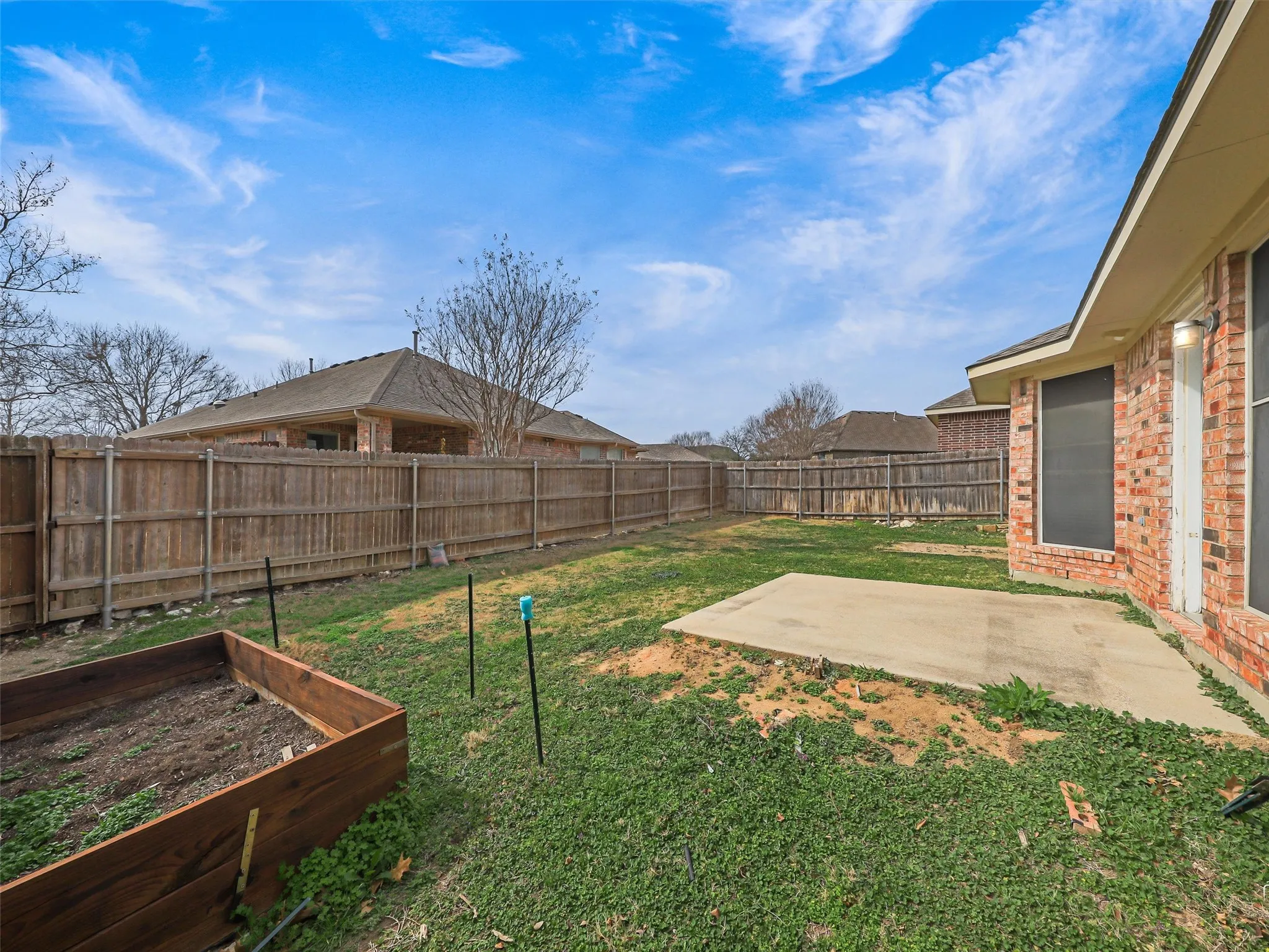 Expansive backyard featuring a wood privacy fence, concrete patio, and an elevated garden bed