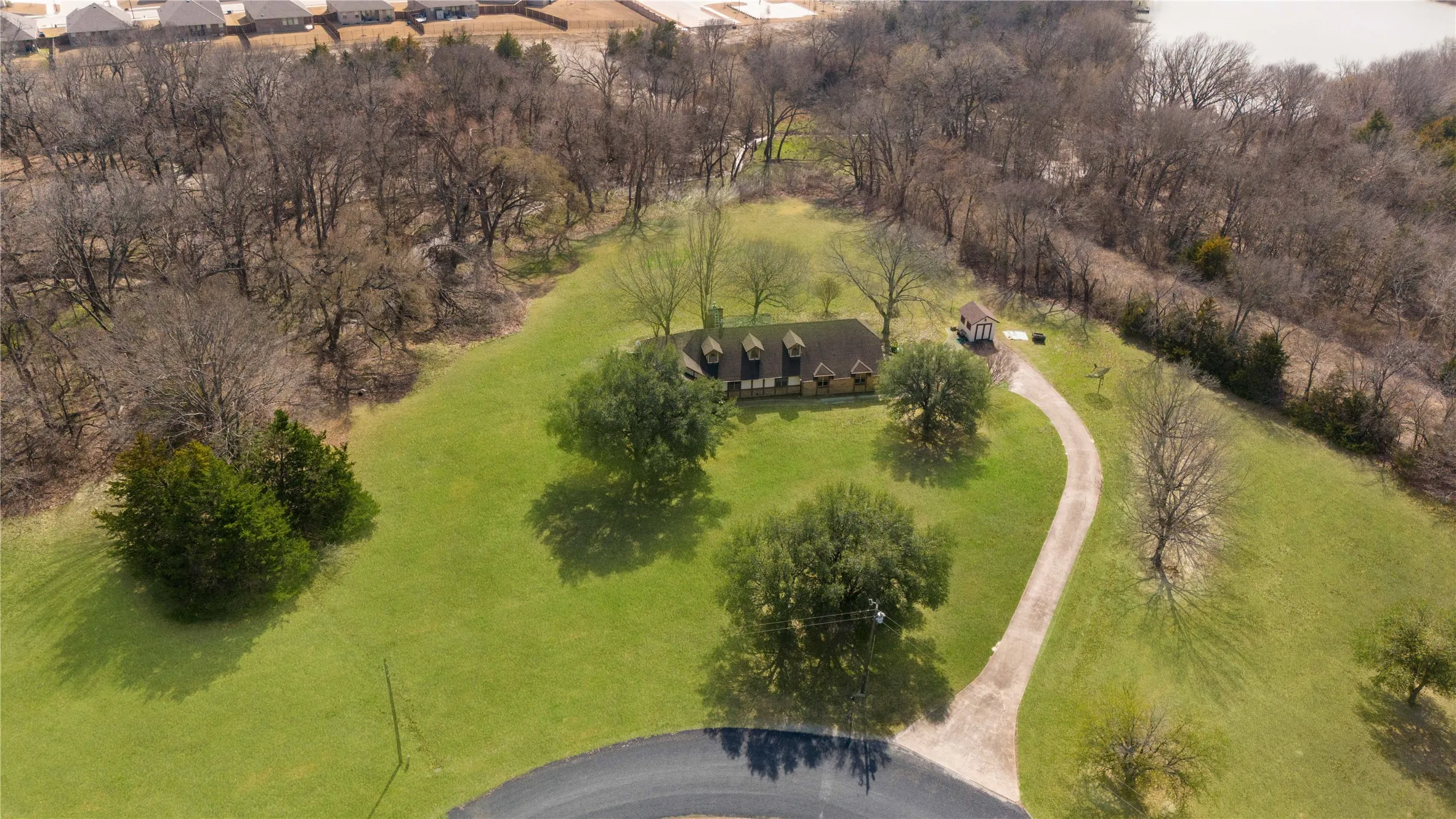 Expansive green lawn, mature trees, winding driveway, and a residential structure with dormer windows