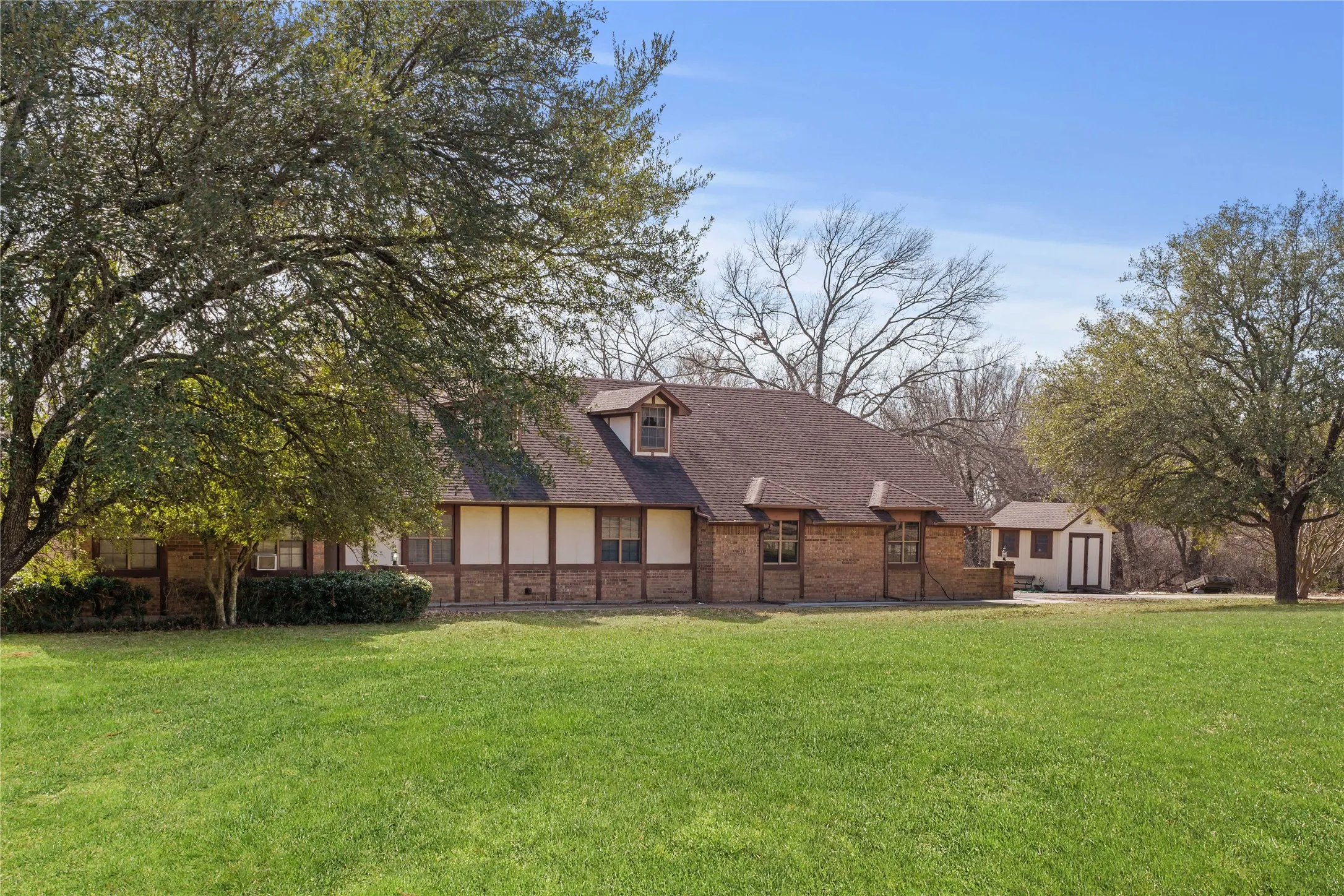 Exterior featuring a brick and stucco finish, brown shingle roof, dormer window, and a detached outbuilding