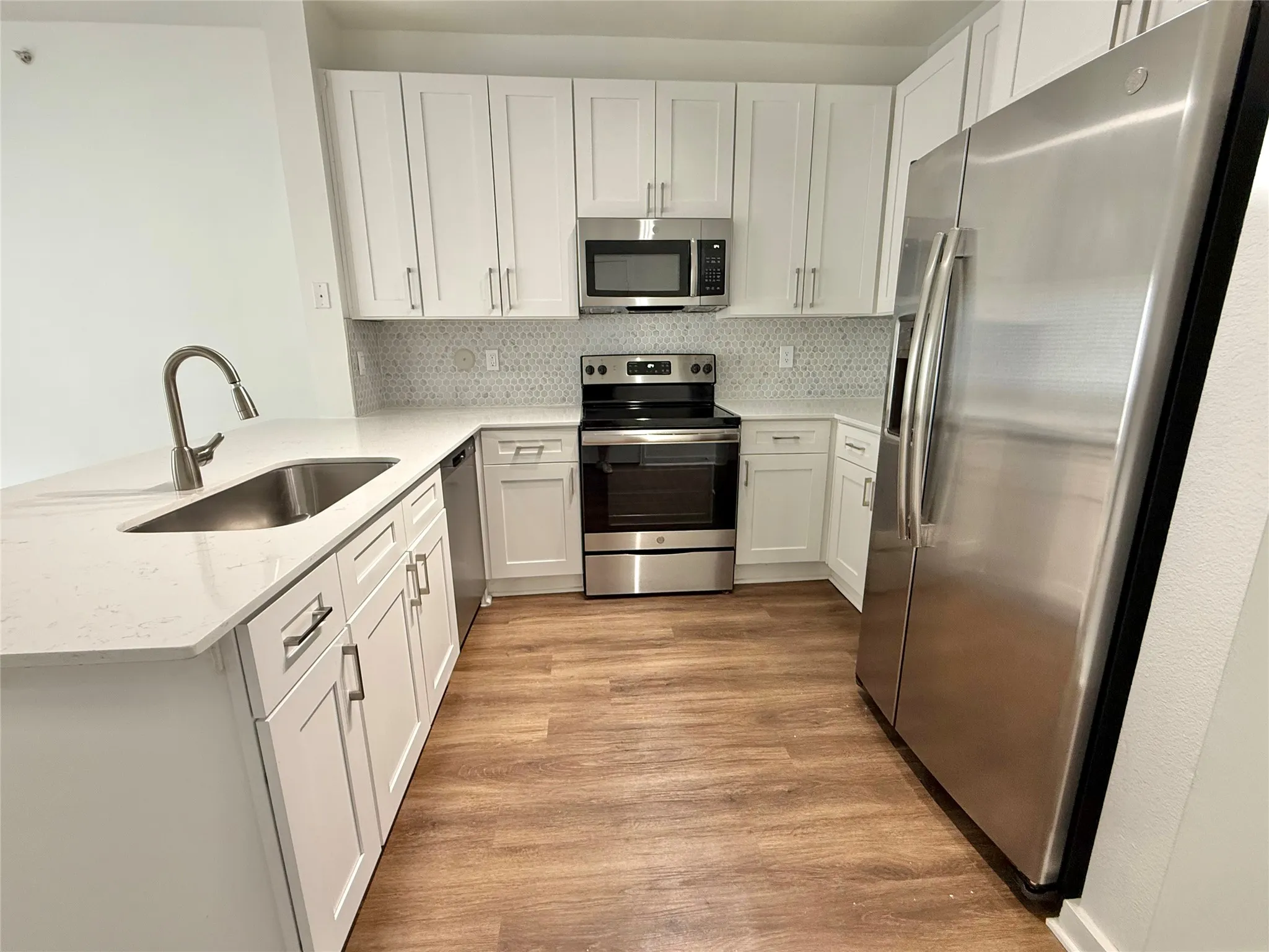 Kitchen featuring appliances with stainless steel finishes, a sink, a peninsula, light wood-style flooring, and backsplash