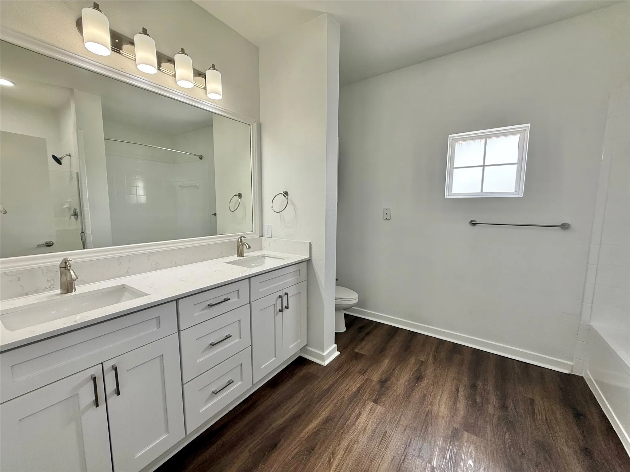 Full bath featuring double vanity, toilet, wood finished floors, and baseboards