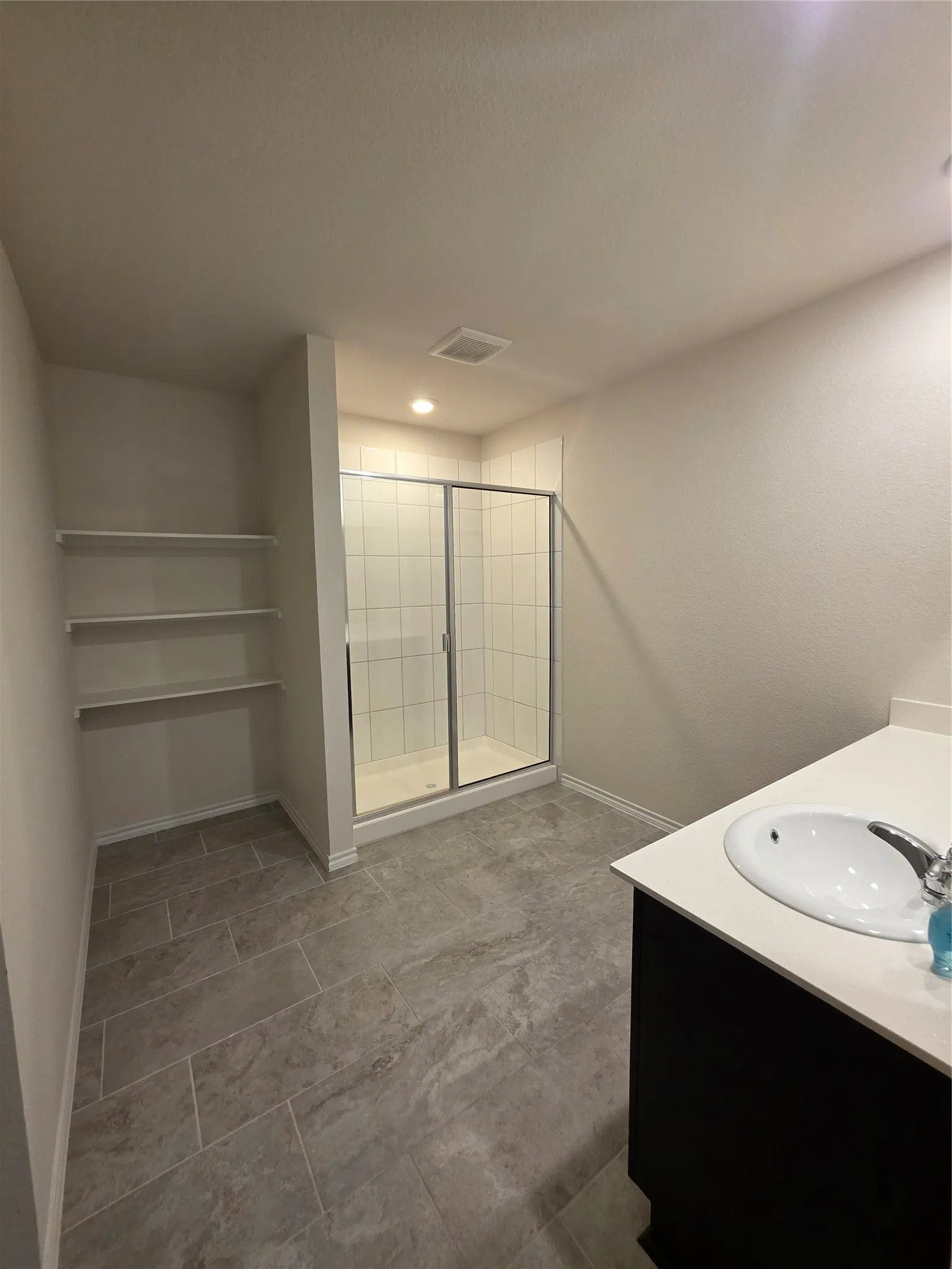Modern bathroom with tiled flooring, a glass-enclosed shower, a vanity featuring a built-in sink, and integrated shelving