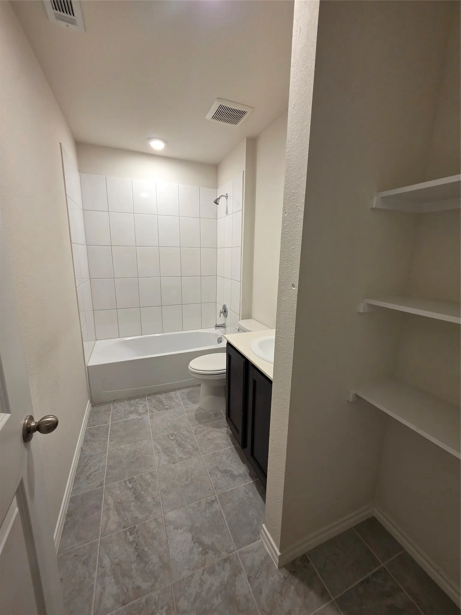 Bathroom featuring a white bathtub with subway tile surround, dark wood-finish vanity with an integrated sink, and large format tile flooring