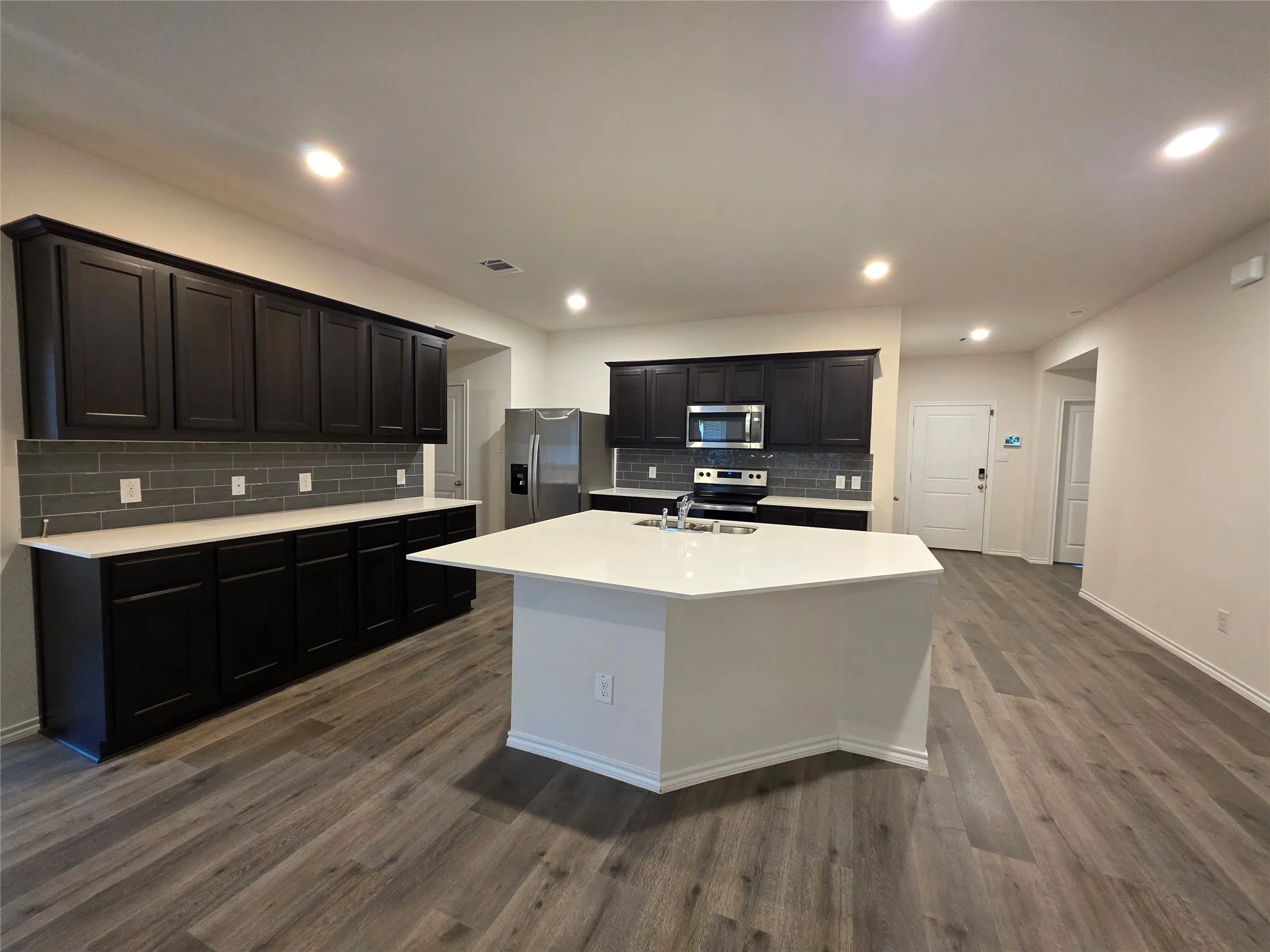 Gourmet kitchen featuring a large central island with white countertops, dark cabinetry, and a subway tile backsplash