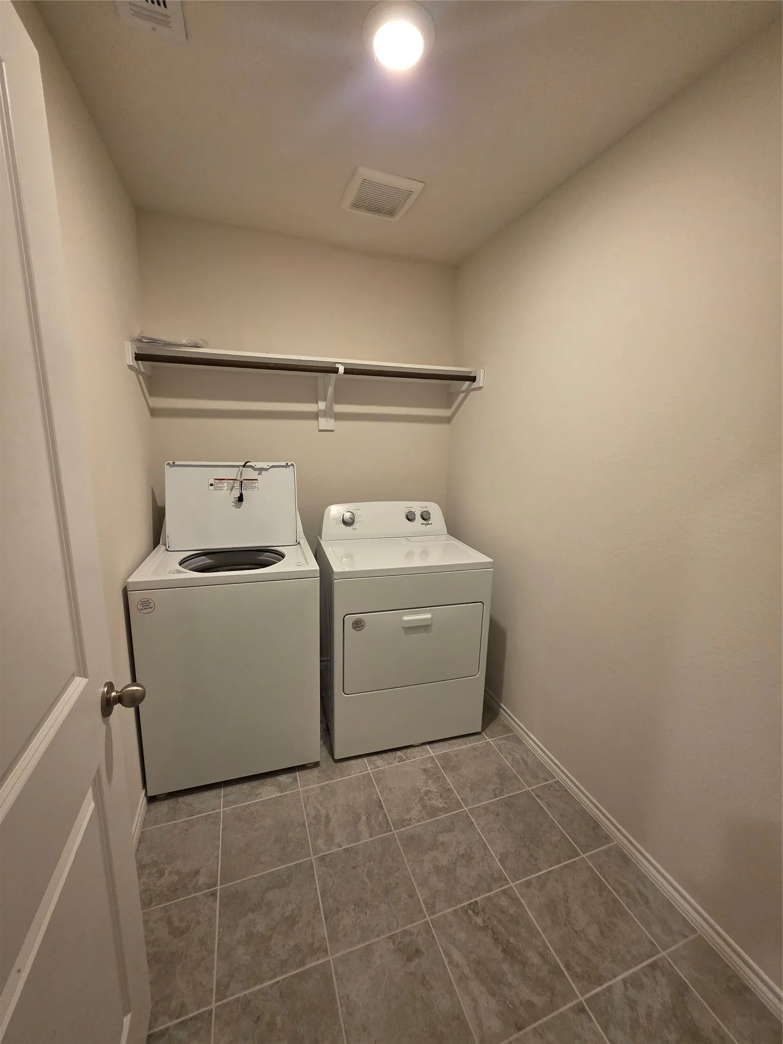 Dedicated laundry area featuring ceramic tile flooring, a wall-mounted shelving unit, and overhead lighting