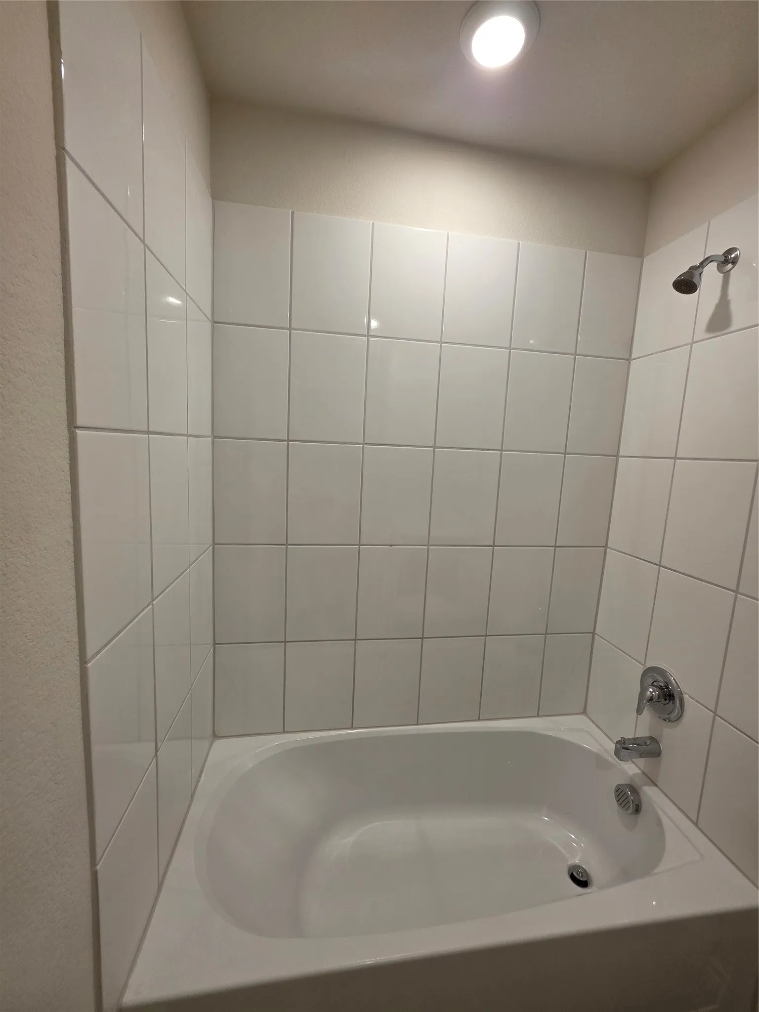 White tile-surround bathtub featuring a polished chrome showerhead and faucet