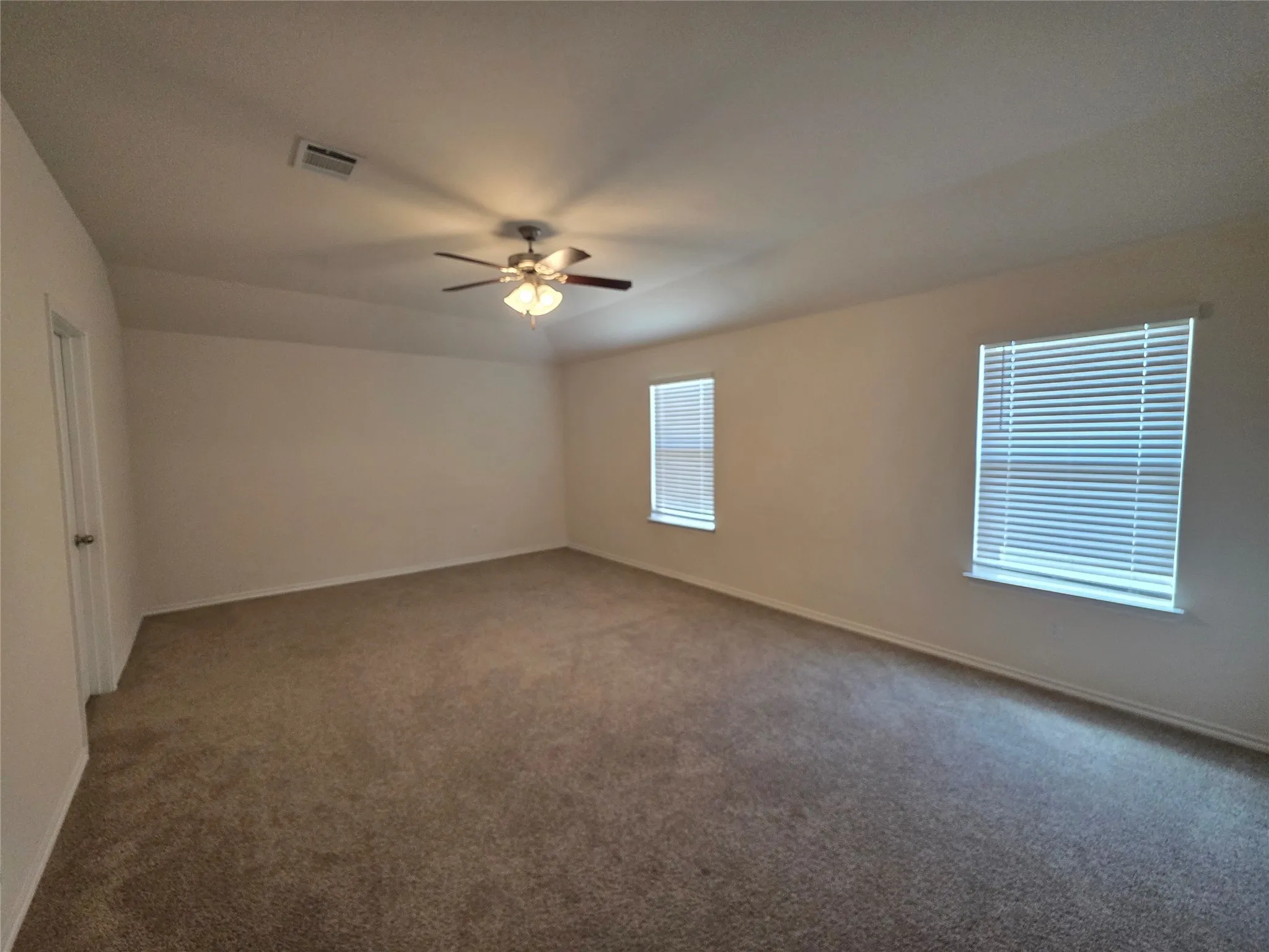 Spacious room featuring neutral carpeting, a ceiling fan with integrated lighting, and multiple windows with blinds