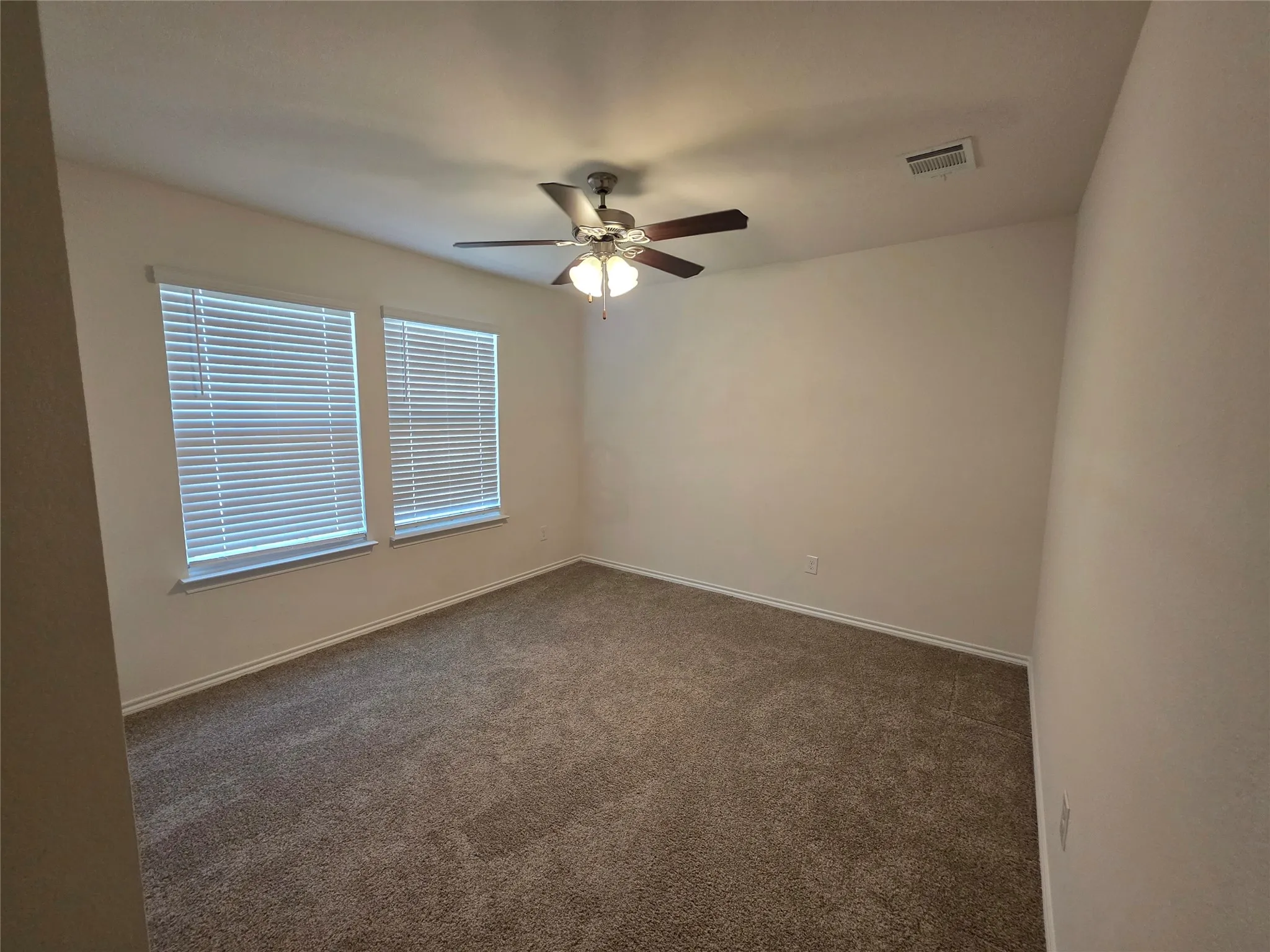 Carpeted room featuring dual windows with blinds and a ceiling fan