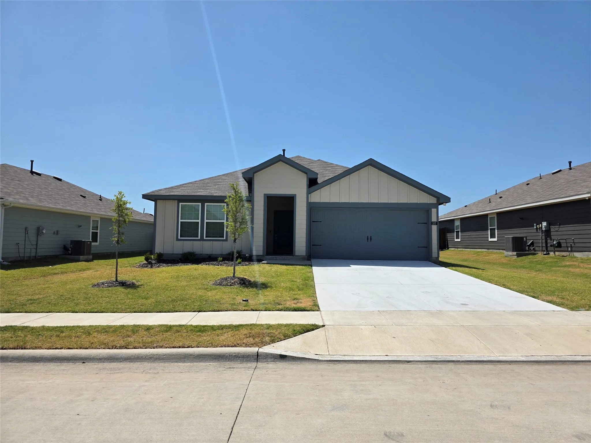 Single-story residence featuring a two-car garage, concrete driveway, and a front yard with young trees