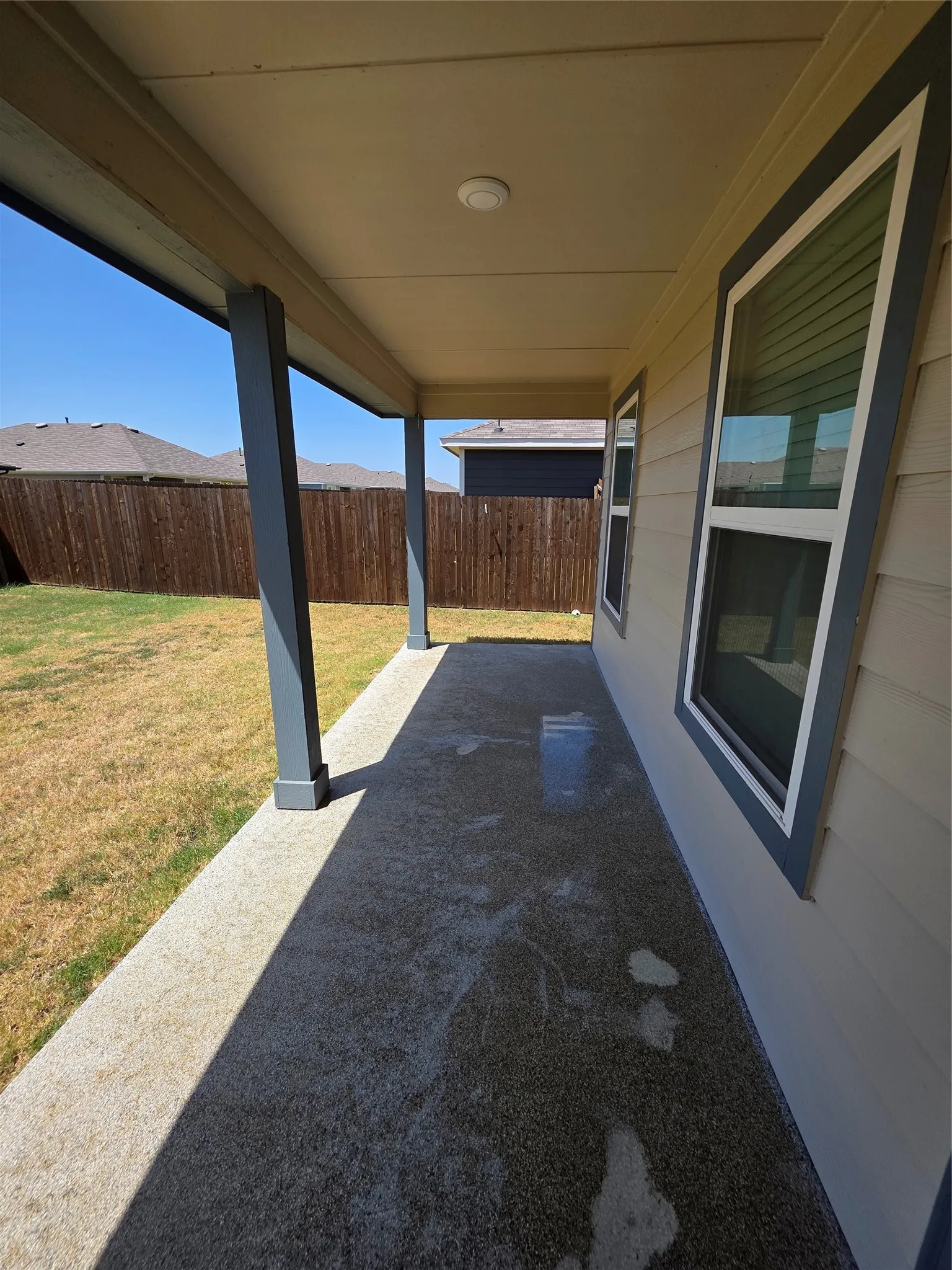 Covered concrete patio with recessed lighting, complemented by a wood-paneled fence