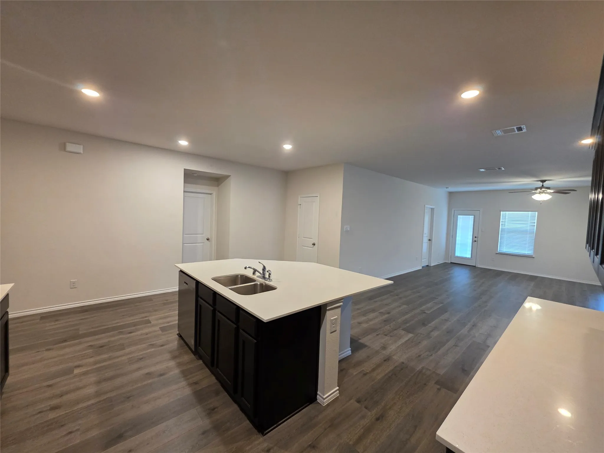 Open-concept living space featuring a large kitchen island with white quartz countertop and dark cabinetry, wood-finish flooring throughout, recessed ceiling lighting, and multiple windows providing natural light