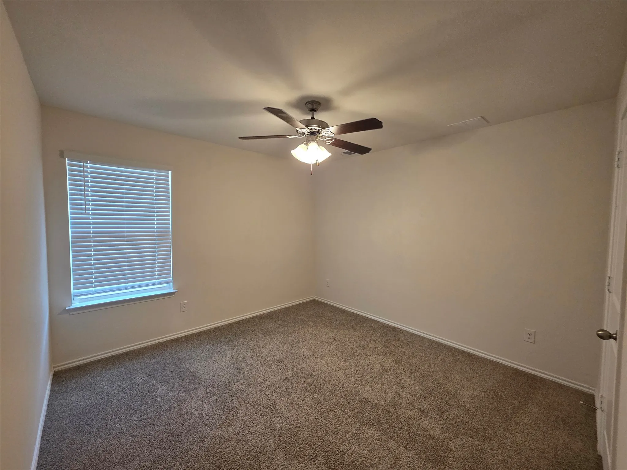 Neutral wall paint, plush carpet flooring, window with blinds, and a ceiling fan with integrated lighting