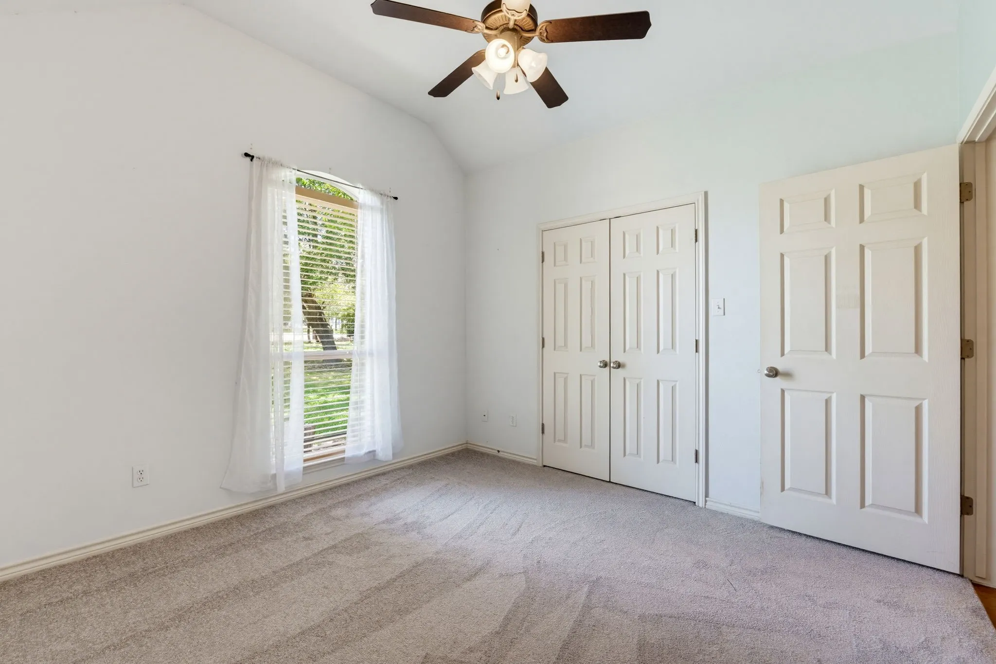 Vaulted ceiling, ceiling fan with light fixture, carpeted flooring, paneled bifold doors, and a paneled entry door