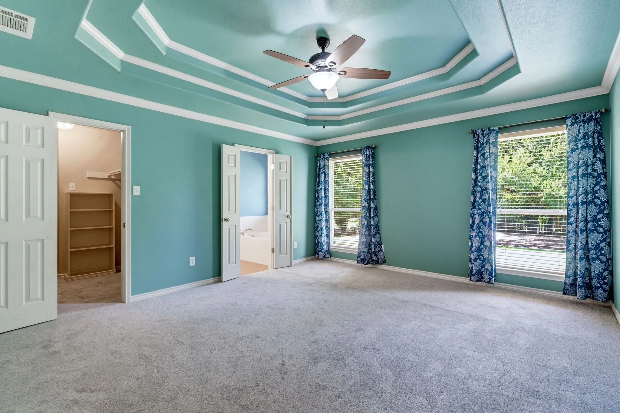 Tray ceiling with decorative molding, ceiling fan, two windows with blinds, and carpeted flooring