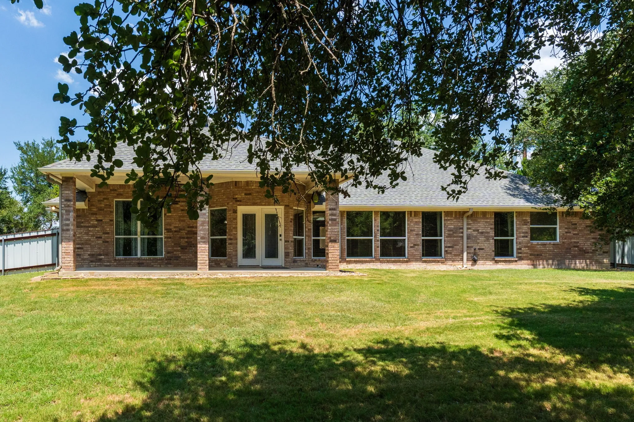 Brick exterior with multiple windows, covered patio, and double glass doors