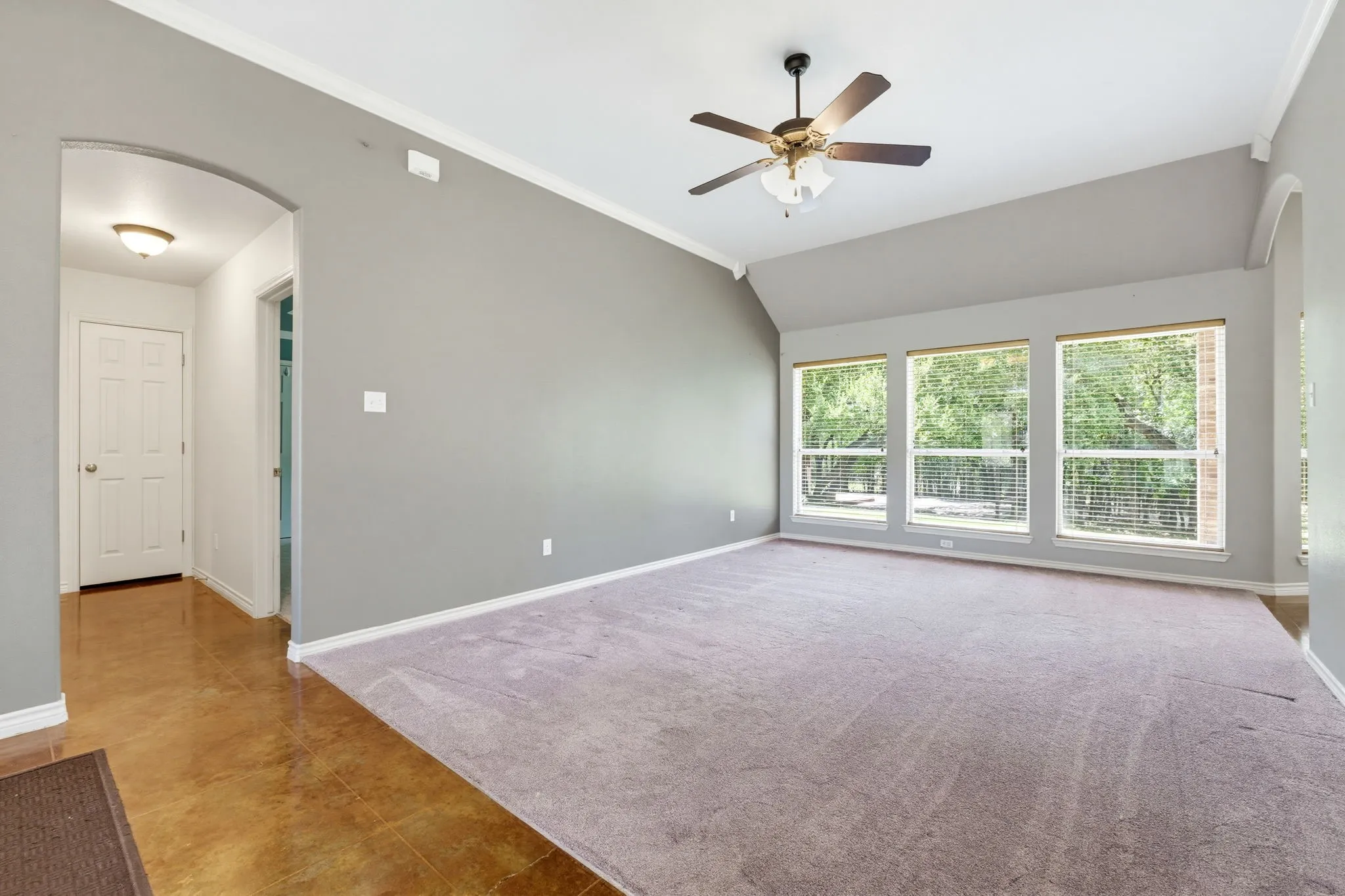 Vaulted ceiling, ceiling fan, three large windows, arched doorway, and wood-finish flooring