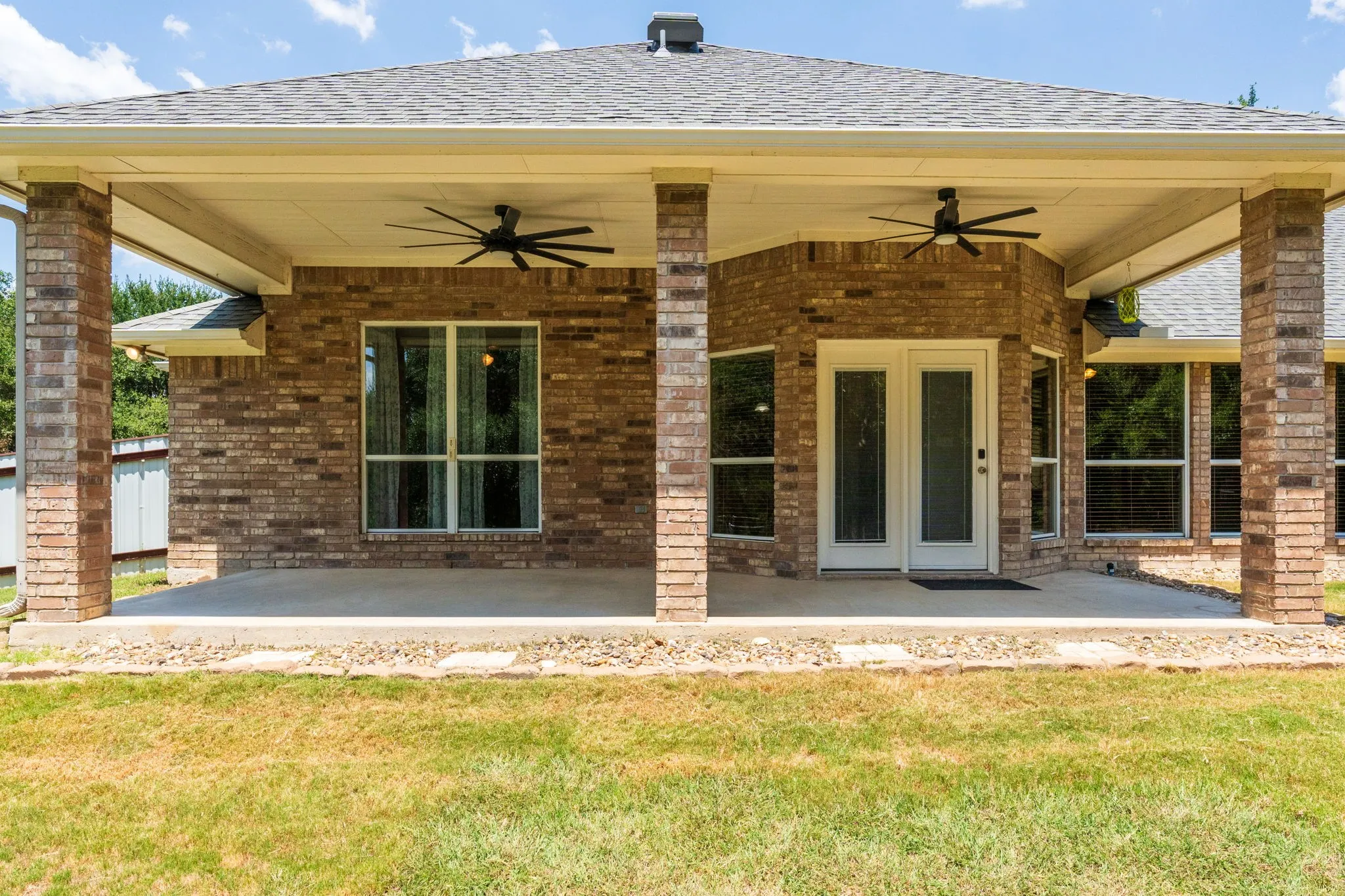 Expansive covered patio featuring brick columns, twin ceiling fans, and a double-door entry