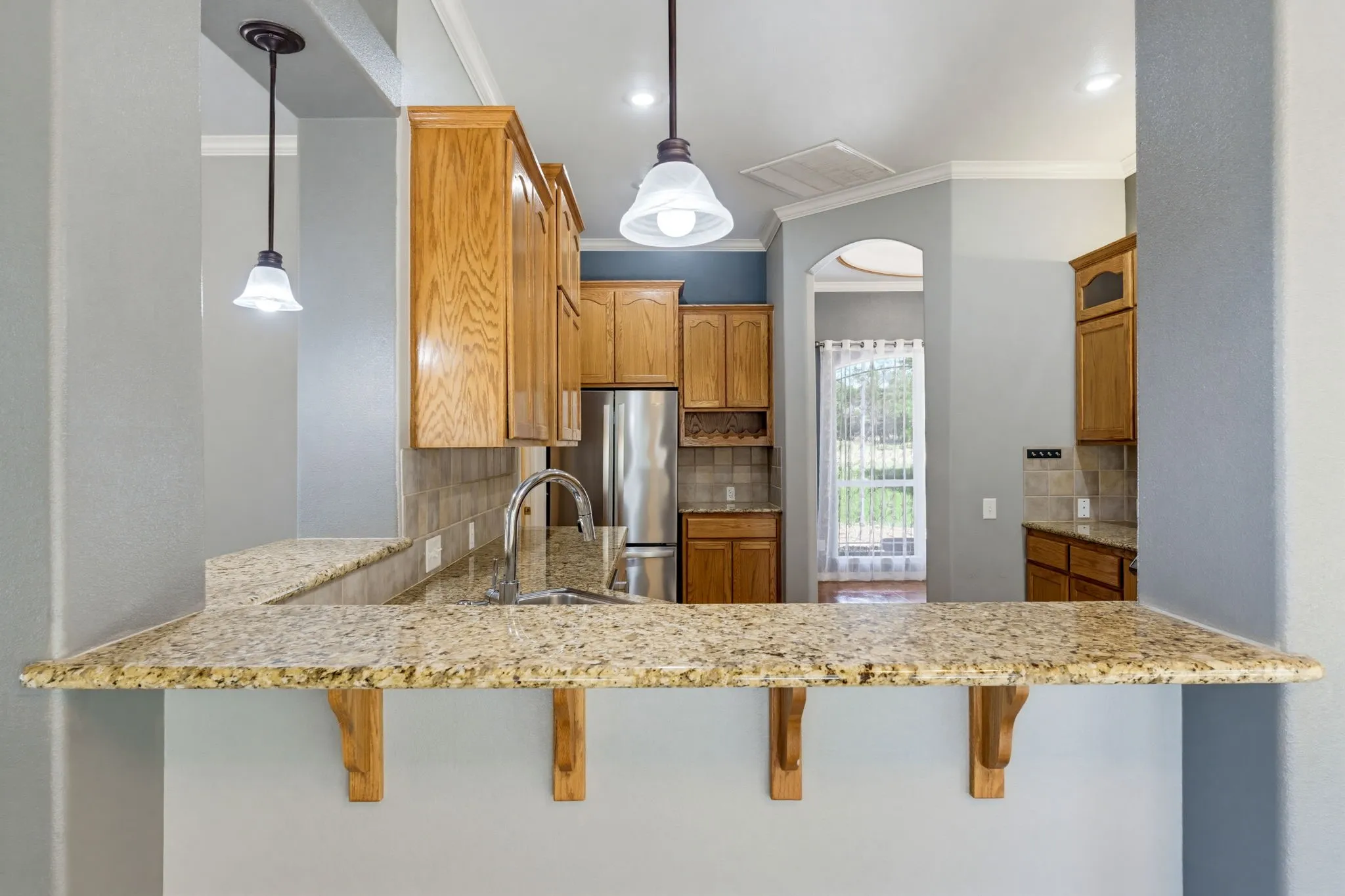 Granite countertops, pendant lighting, wood cabinetry, stainless steel refrigerator, and a tile backsplash