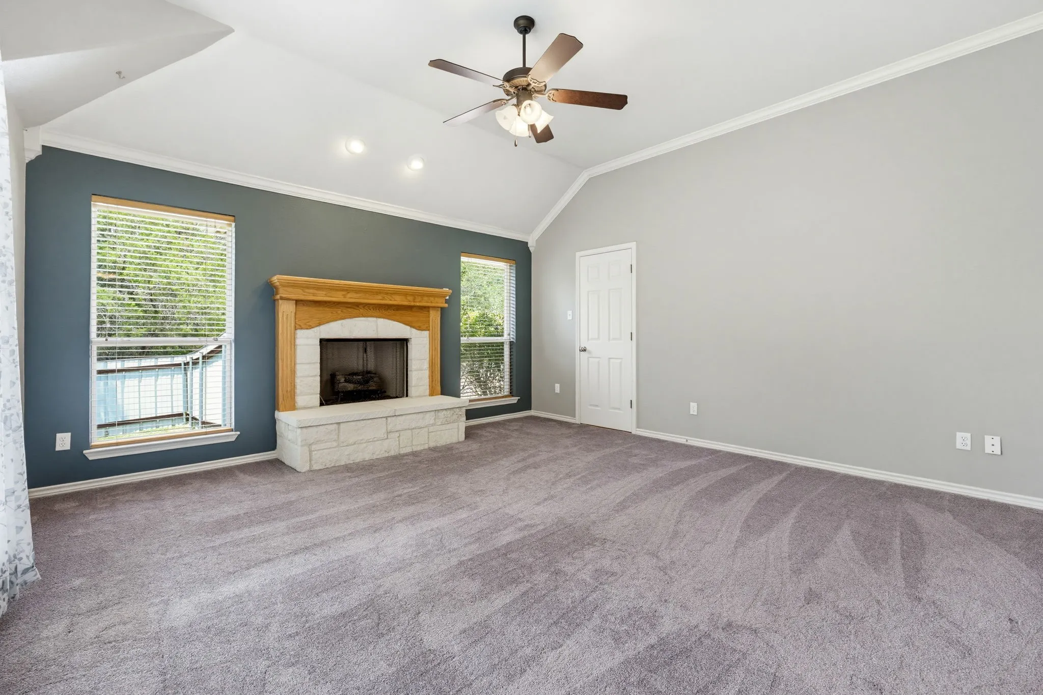 Vaulted ceiling with an attached ceiling fan, recessed lighting, wood-surround fireplace with a stone hearth, and carpeted flooring