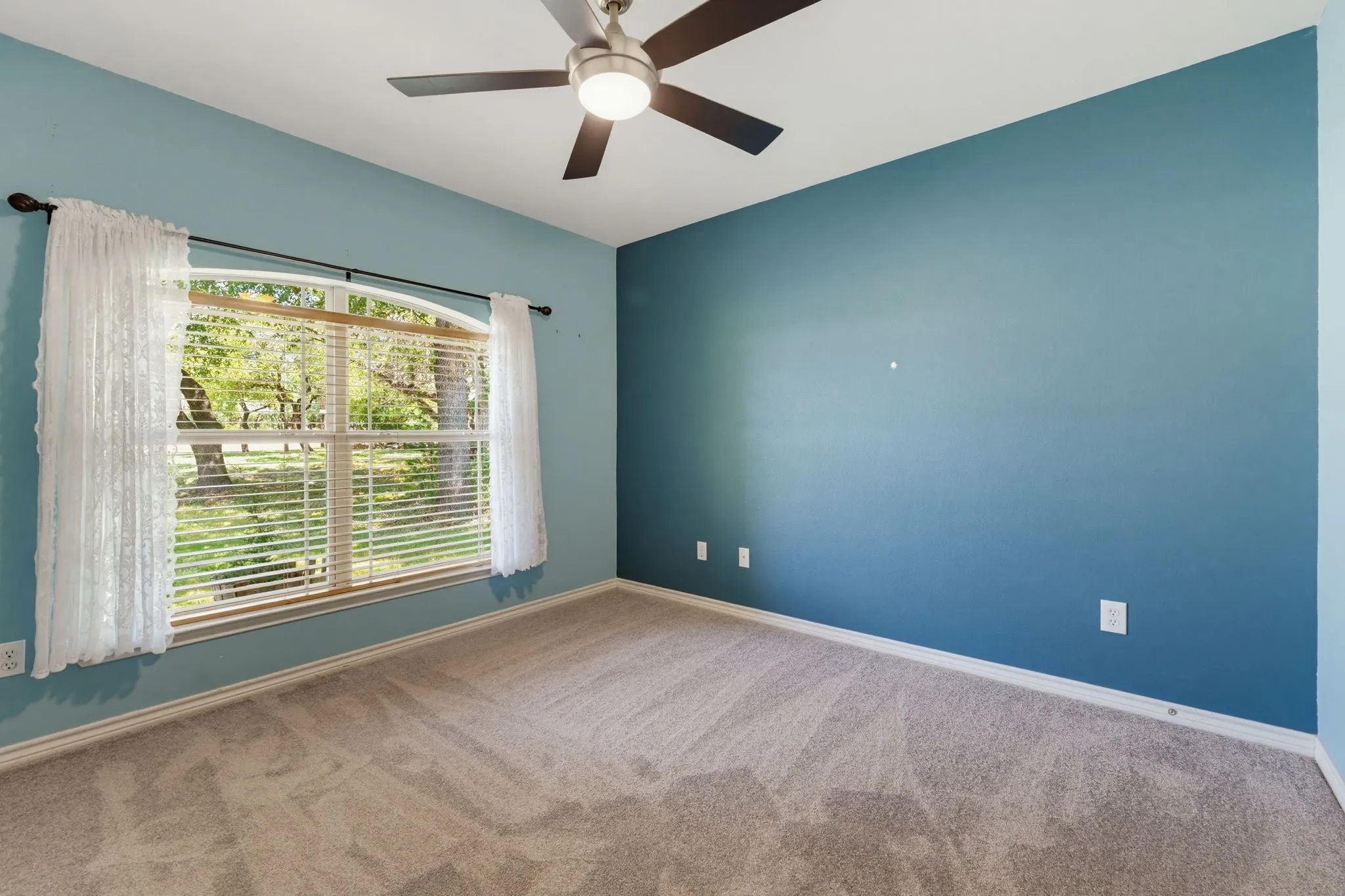 Arched window with blinds, carpet flooring, ceiling fan with integrated lighting, and painted walls