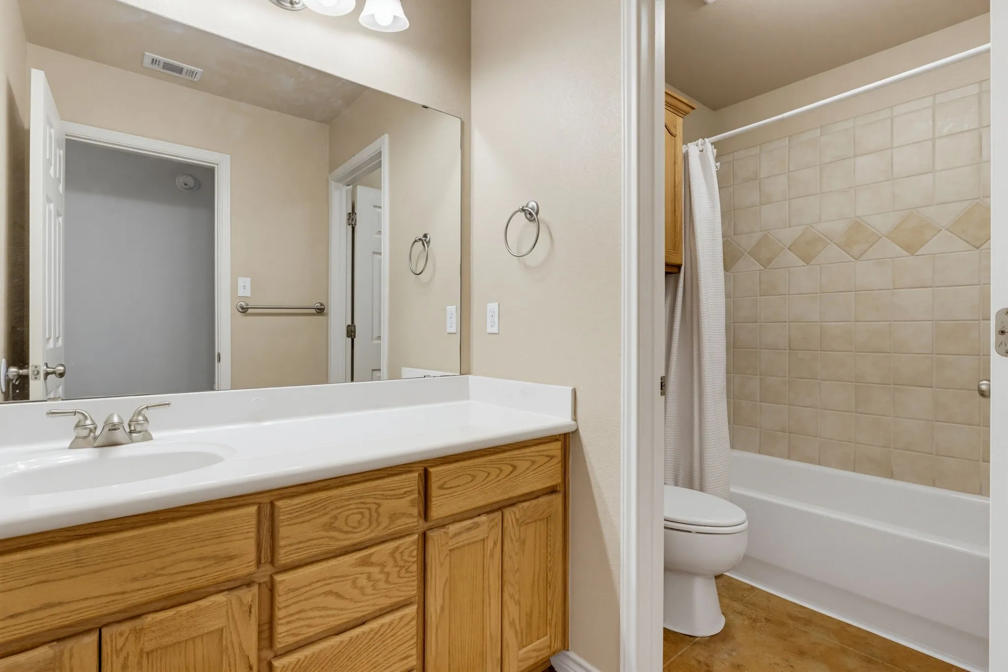 Bathroom featuring a wood-finish vanity with a white countertop, an integrated sink, and a large wall mirror