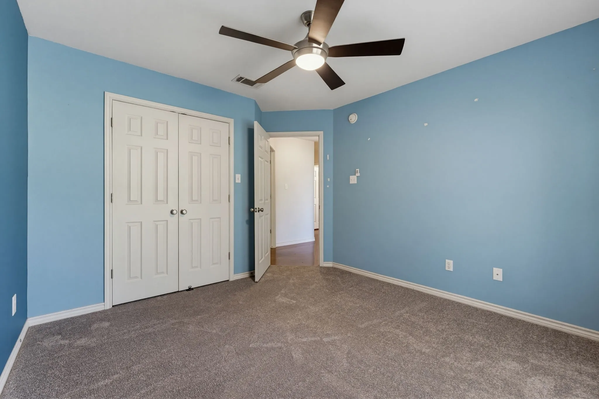 Spacious bedroom with soft blue walls, neutral carpeting, ceiling fan with integrated lighting, and dual closets with six-panel doors