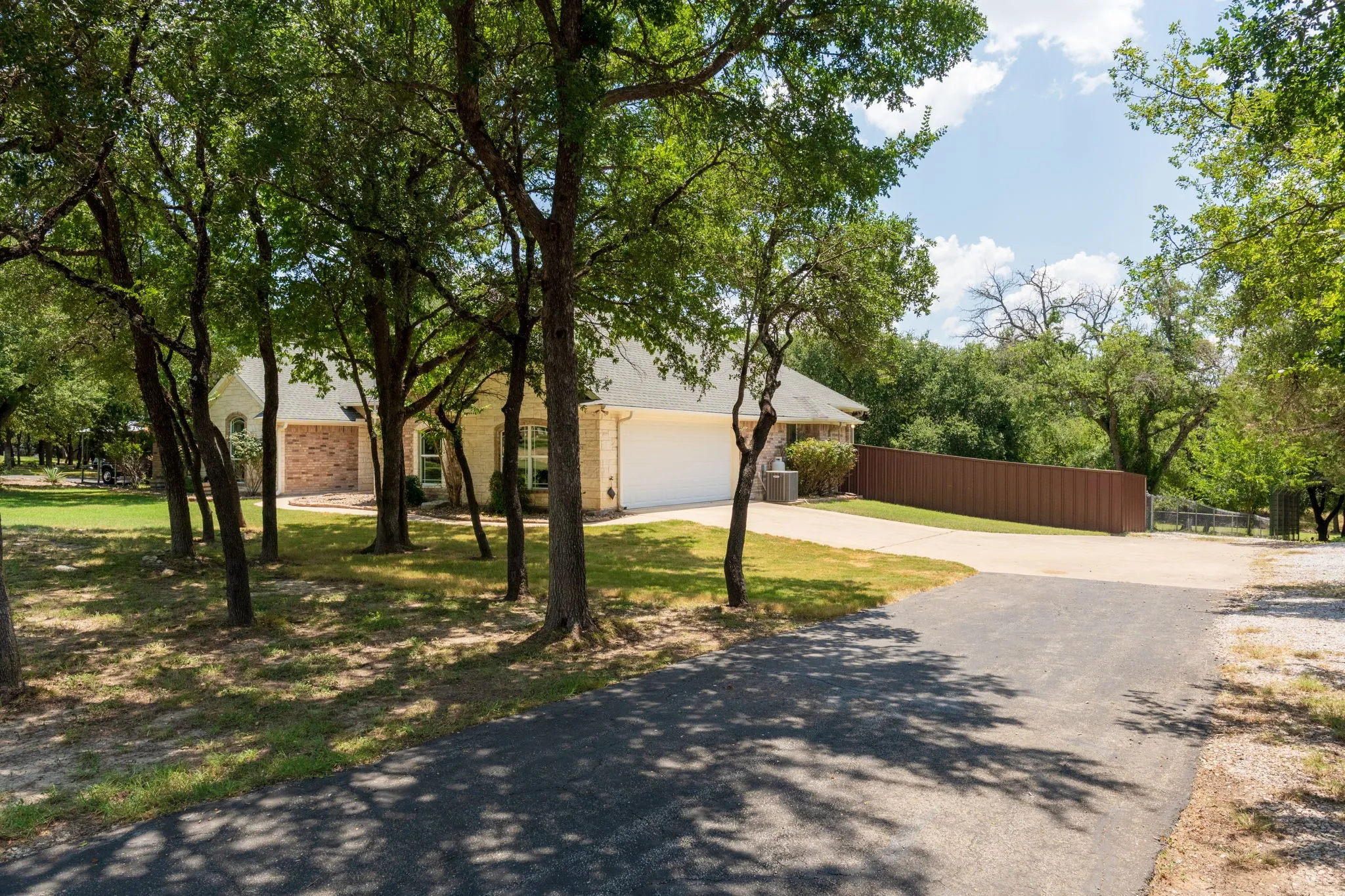 Brick and siding exterior with a shingled roof, featuring a paved driveway and mature trees