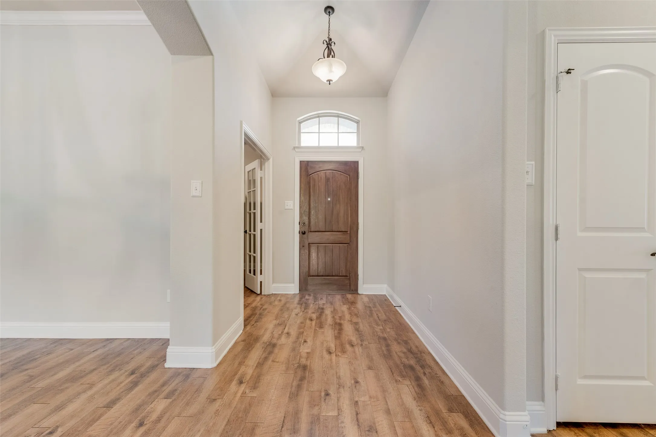 Vaulted entry with wood-finish flooring, an arched transom window, and a decorative pendant light fixture