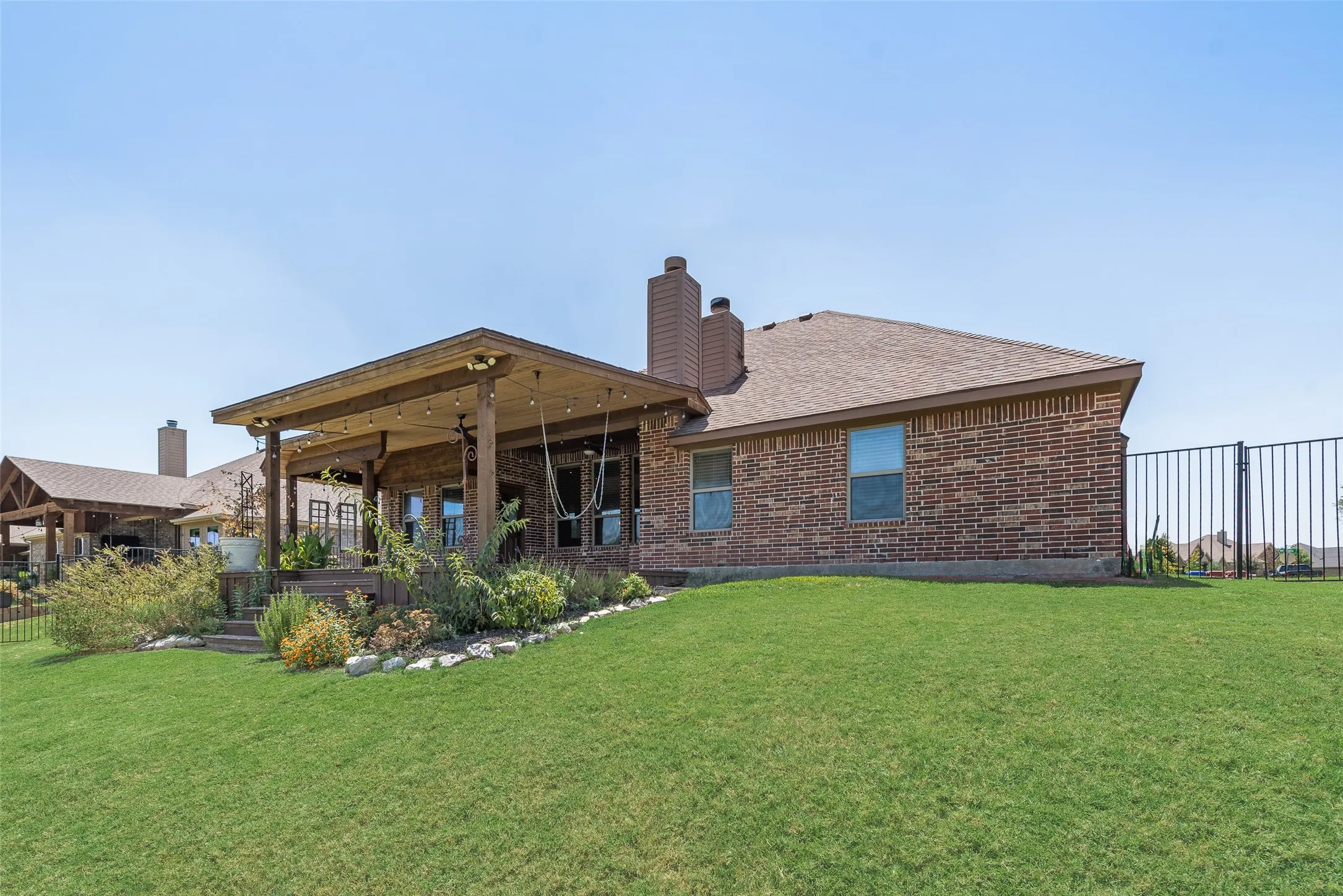 Expansive green lawn with a covered patio featuring exposed wood beams and recessed lighting