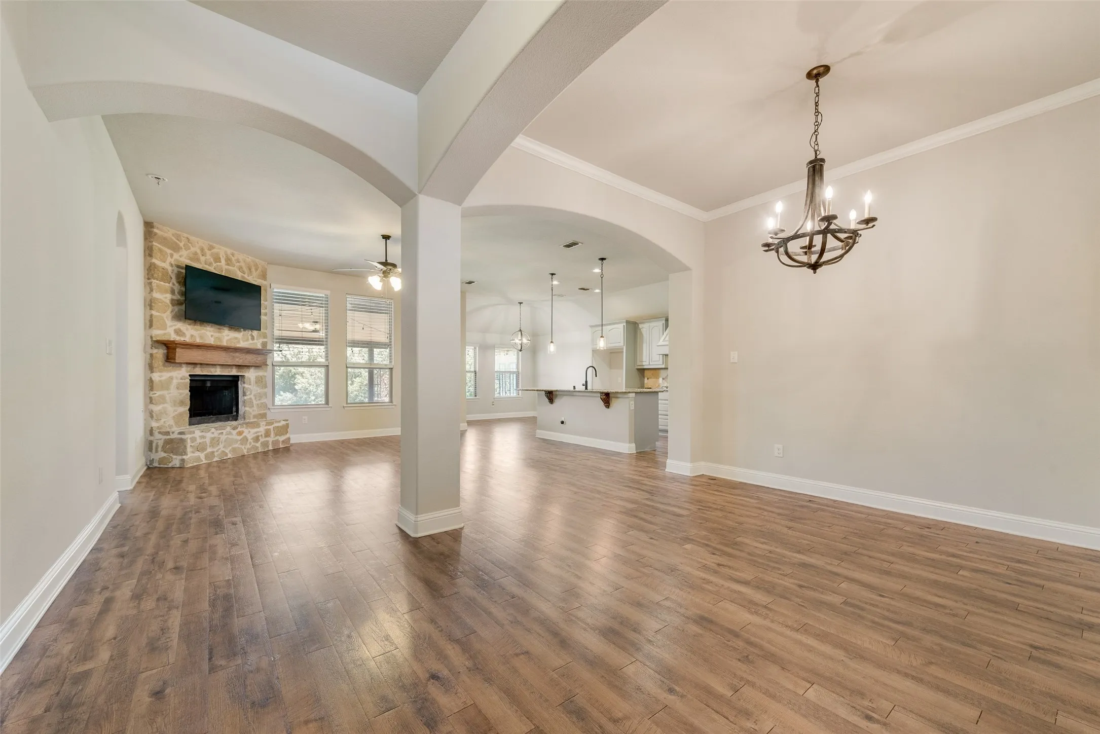 Wood-finish flooring throughout, stone-clad fireplace with mantel, arched doorways, crown molding, and a chandelier