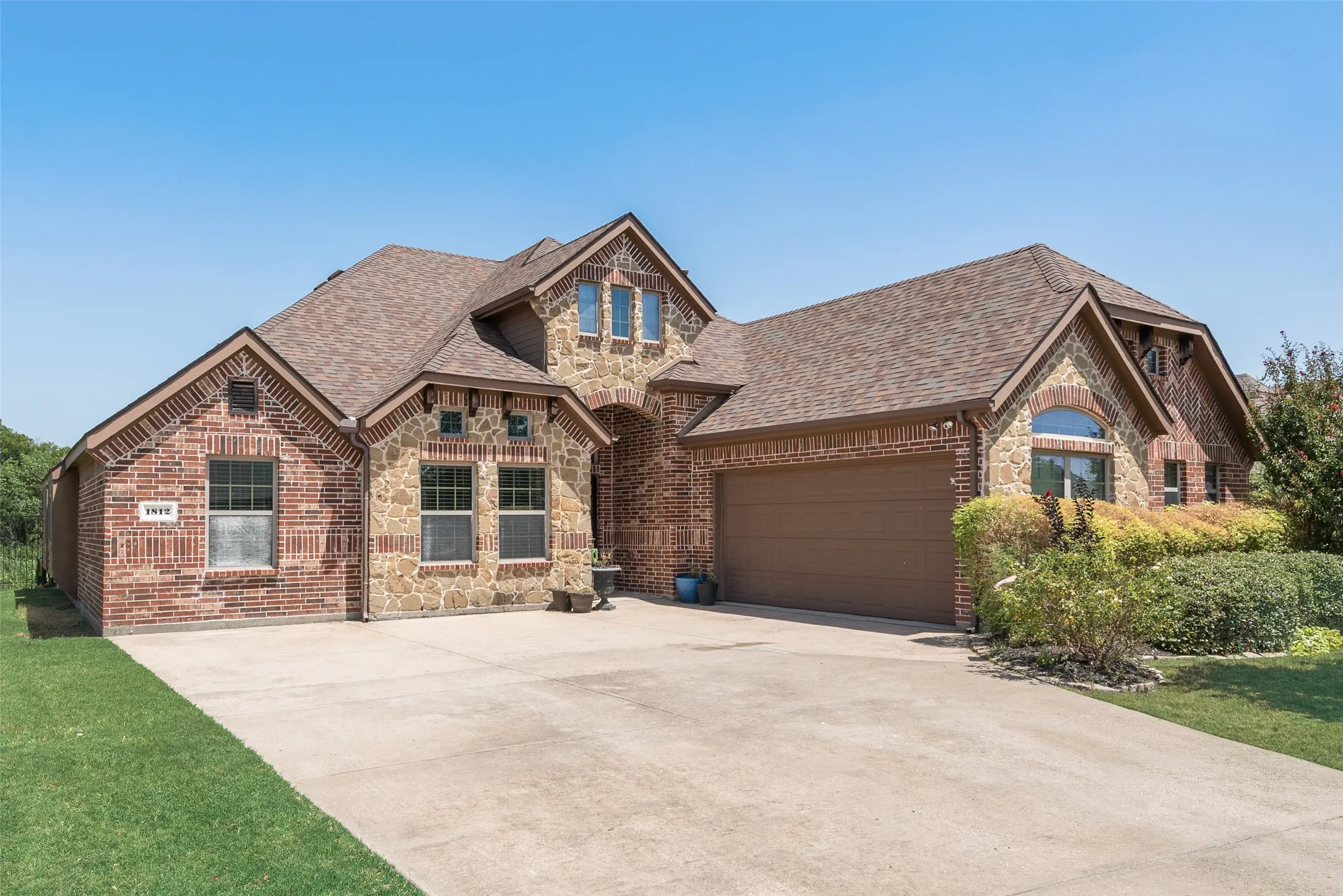 Brick and stone veneer exterior with a gabled roof, attached two-car garage, concrete driveway, and established landscaping